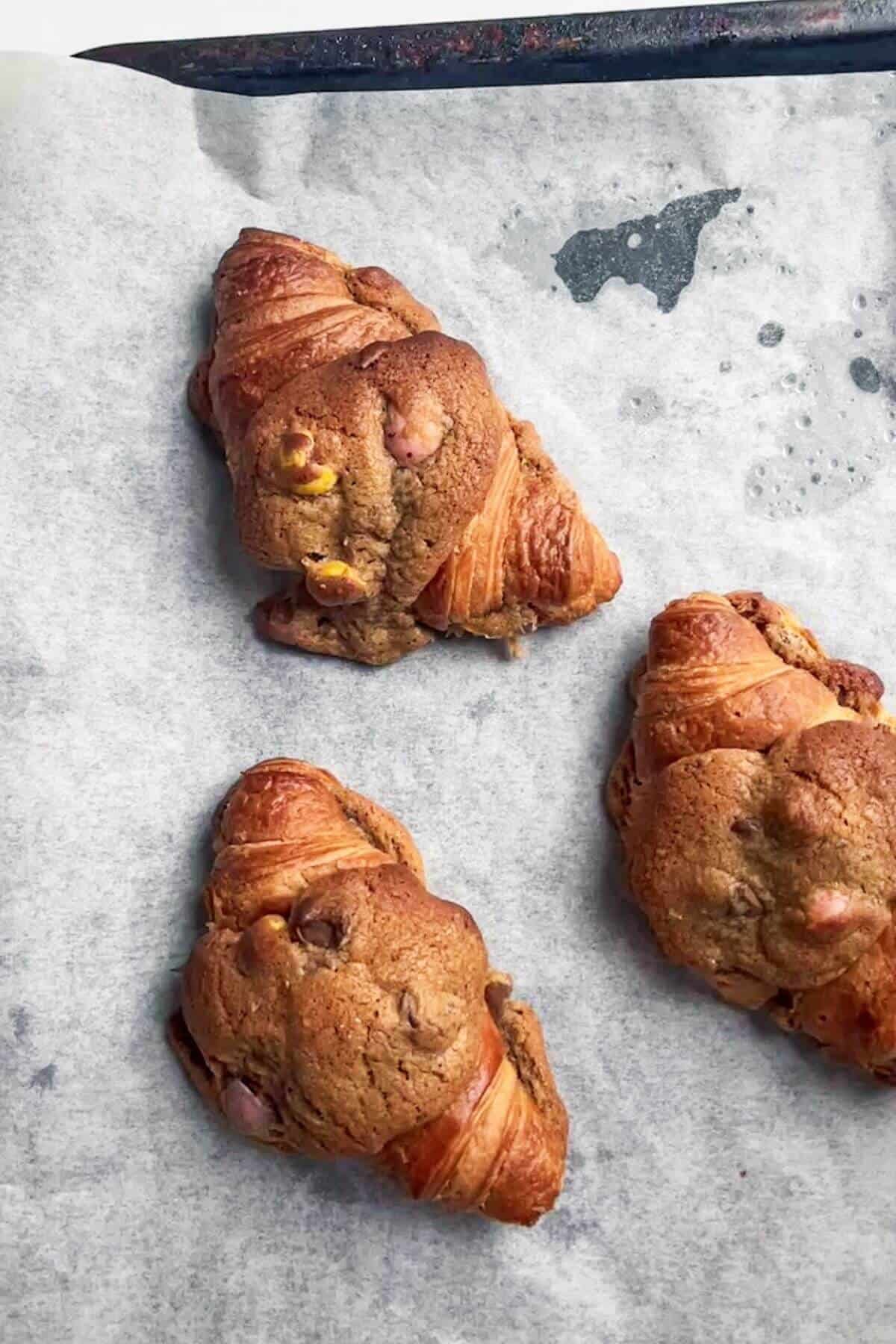 Three baked cookie croissants on a lined baking tray.