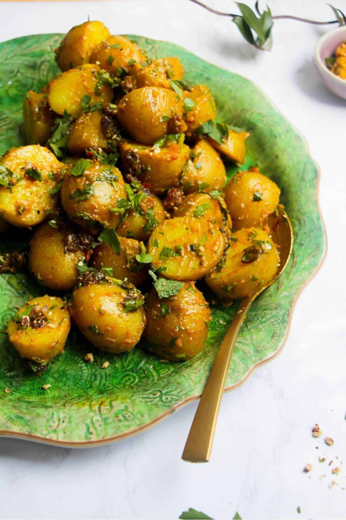 Coronation potato salad on a large green platter with a gold serving spoon and small bowl of coronation sauce on the side.