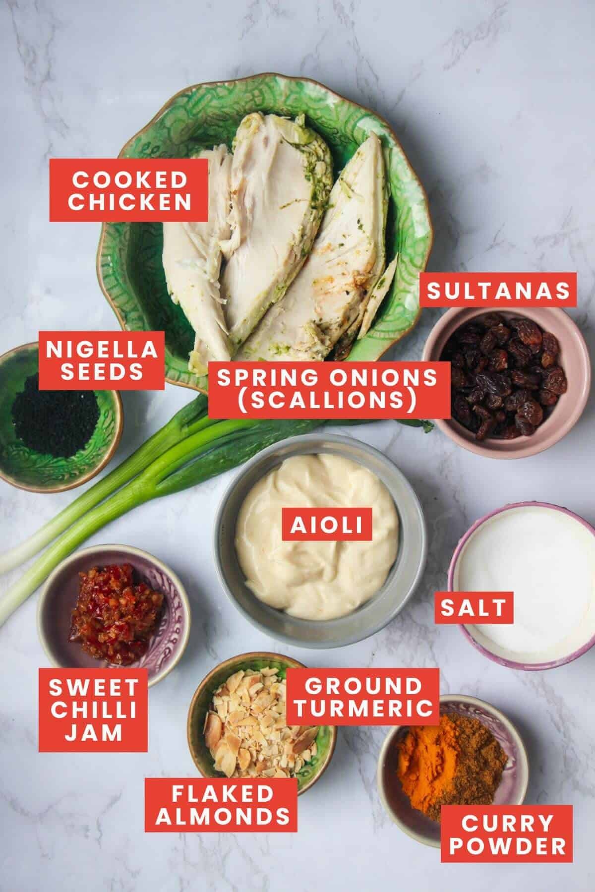 Ingredients for coronation chicken, laid out on a white marble background and labelled.