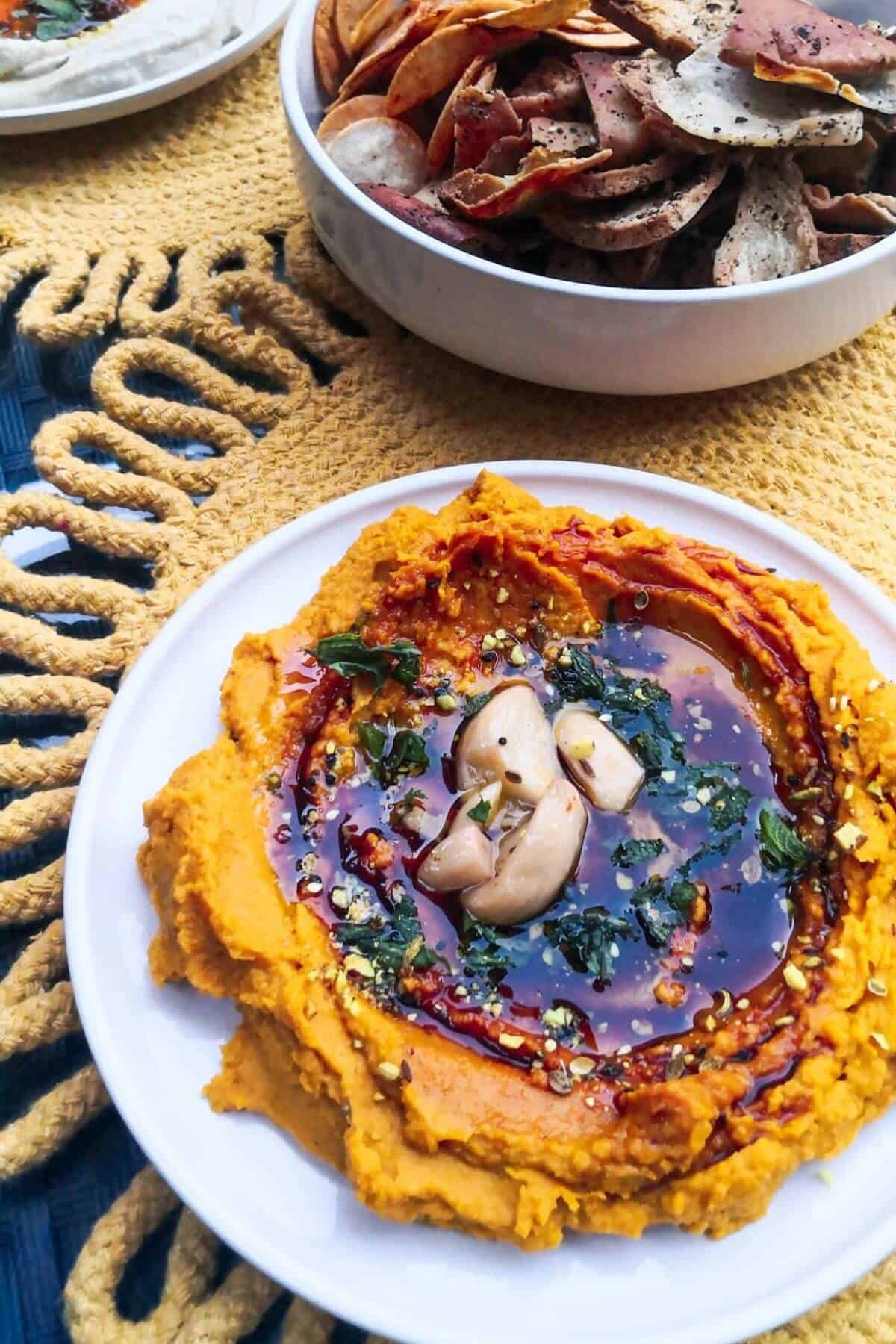Whipped carrot dip on a small white plate with a bowl of crackers in the background.