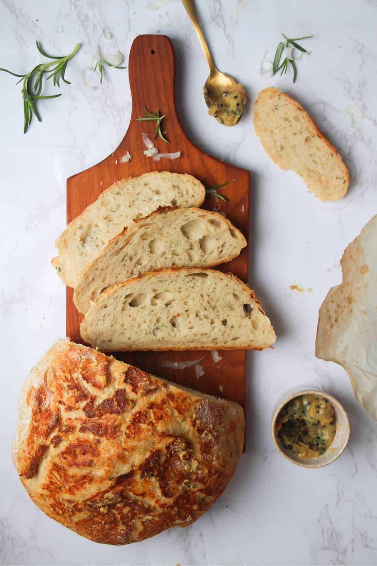 3 slices of bread on a small wooden board with the rest of the loaf and garlic butter in the background.
