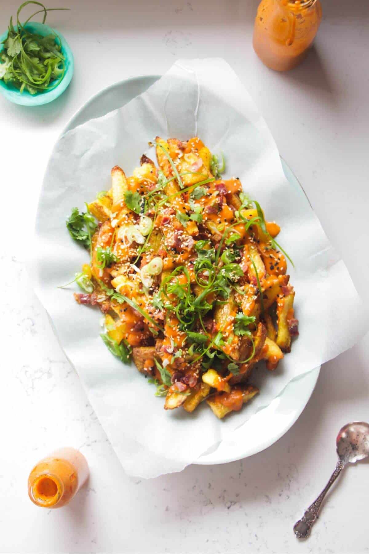 Loaded potato wedges on a large oval white plate with small jug of gochujang bechamel on the side.