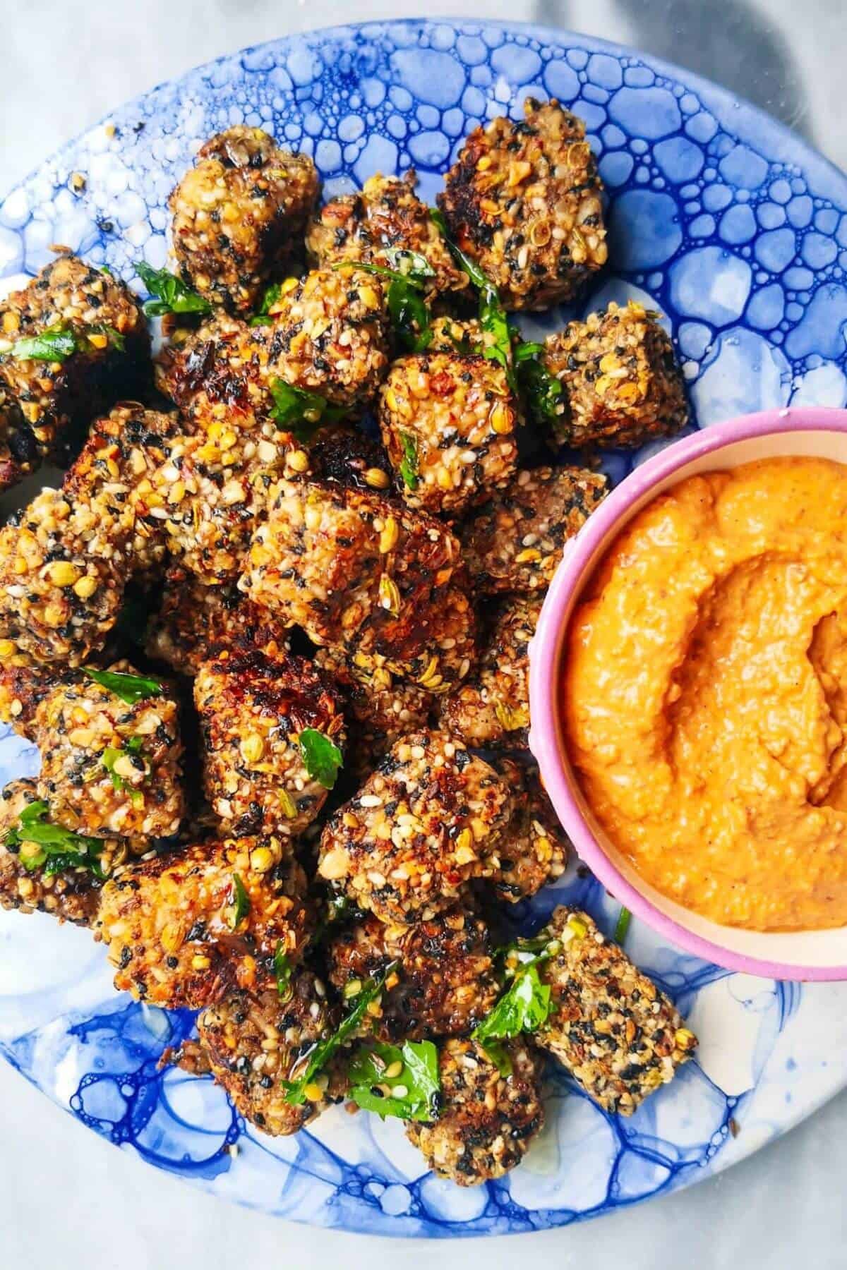 Halloumi bites on a blue marble plate with red pepper sauce on the side.