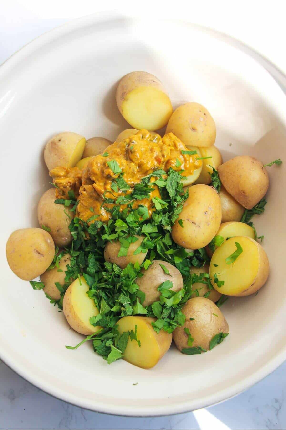 Cooked baby potatoes, green mint and coronation sauce in a large ceramic mixing bowl.