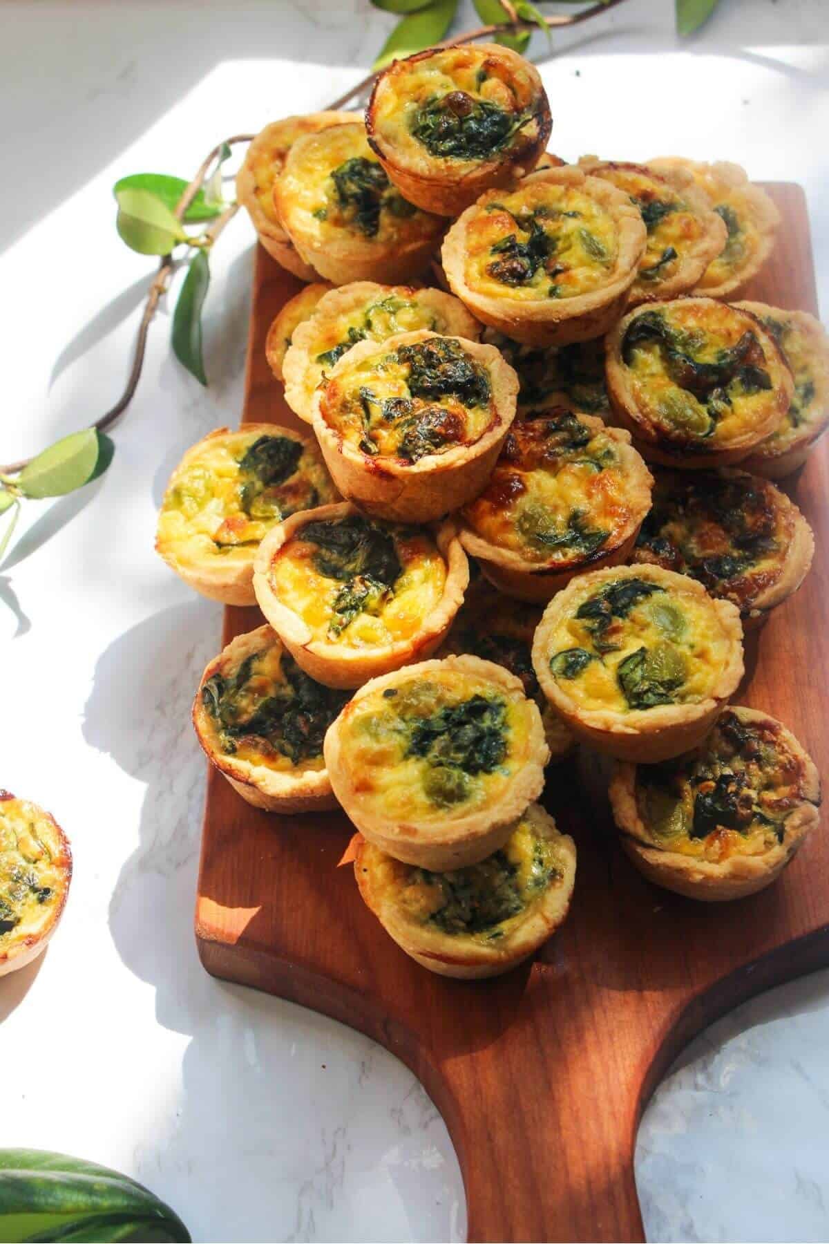 A pile of mini coronation quiches on a small wooden board.