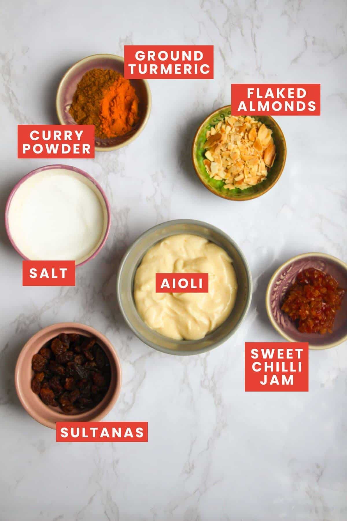 Ingredients for coronation sauce laid out on a white marble background and labelled.