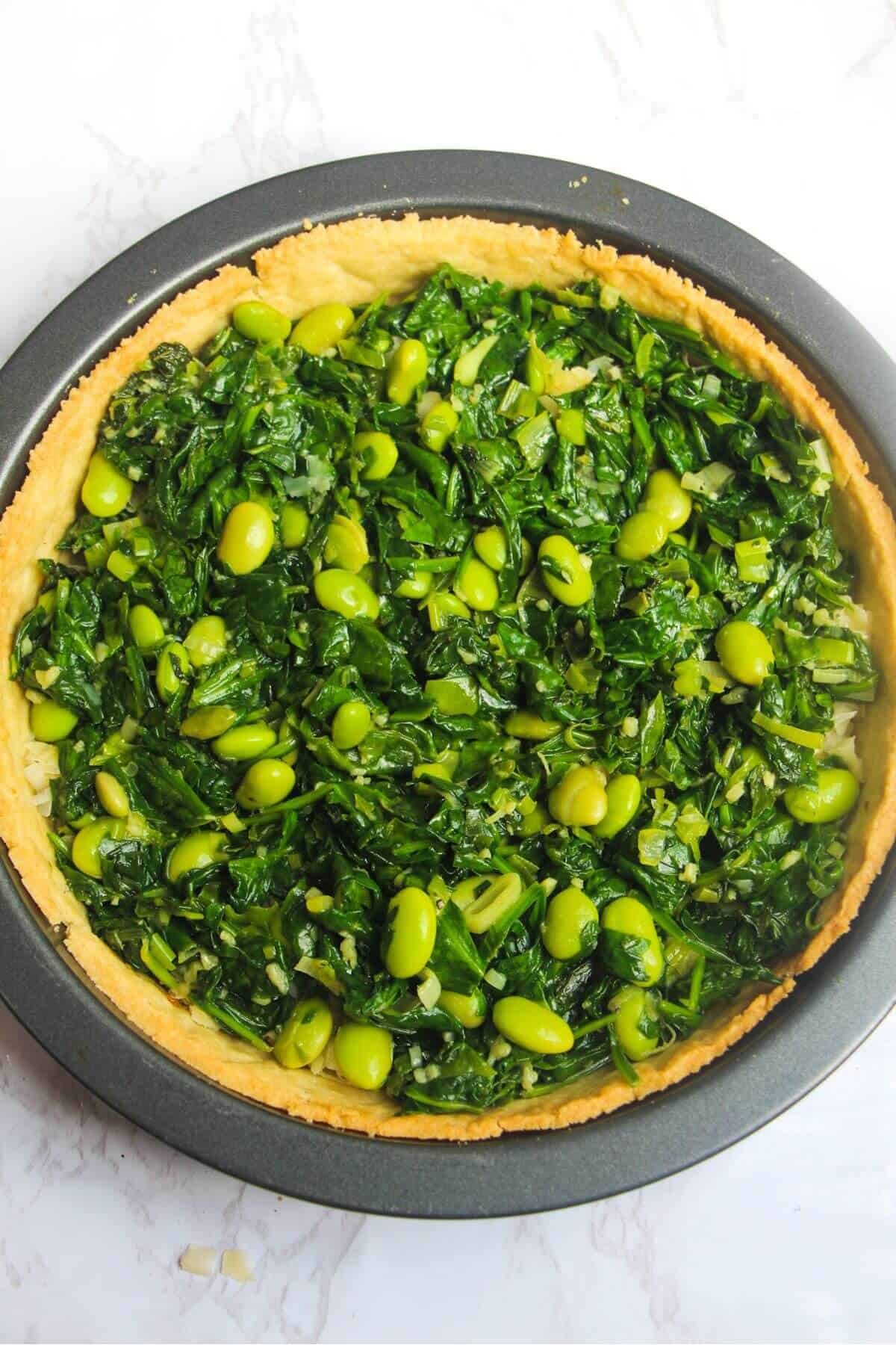 Cooked spinach, edamame beans, spring onions and mint leaves in a blind-baked pastry case in a tin.