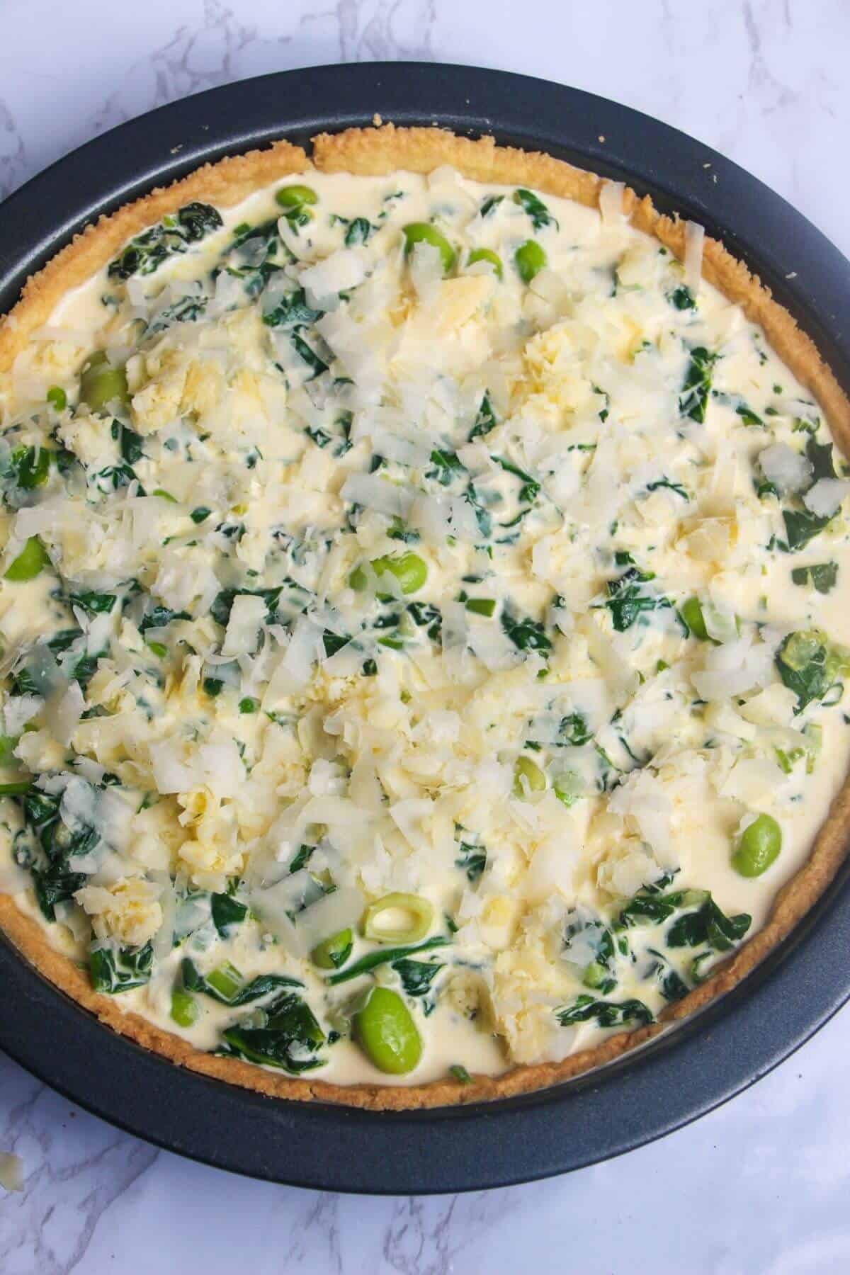 Grated cheese scattered on top of coronation quiche in a tin.