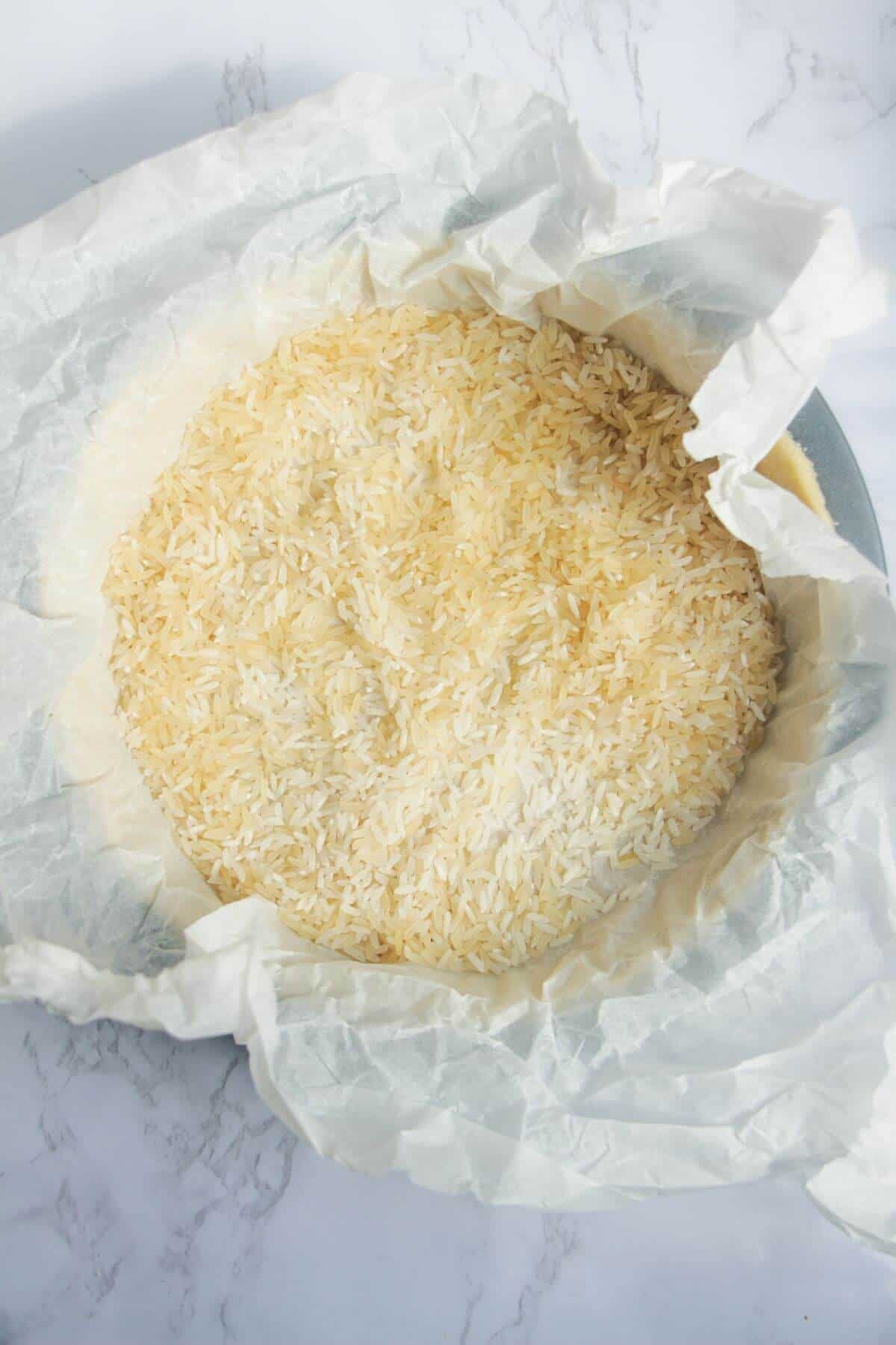 Uncooked rice in baking paper inside pastry in a quiche tin.