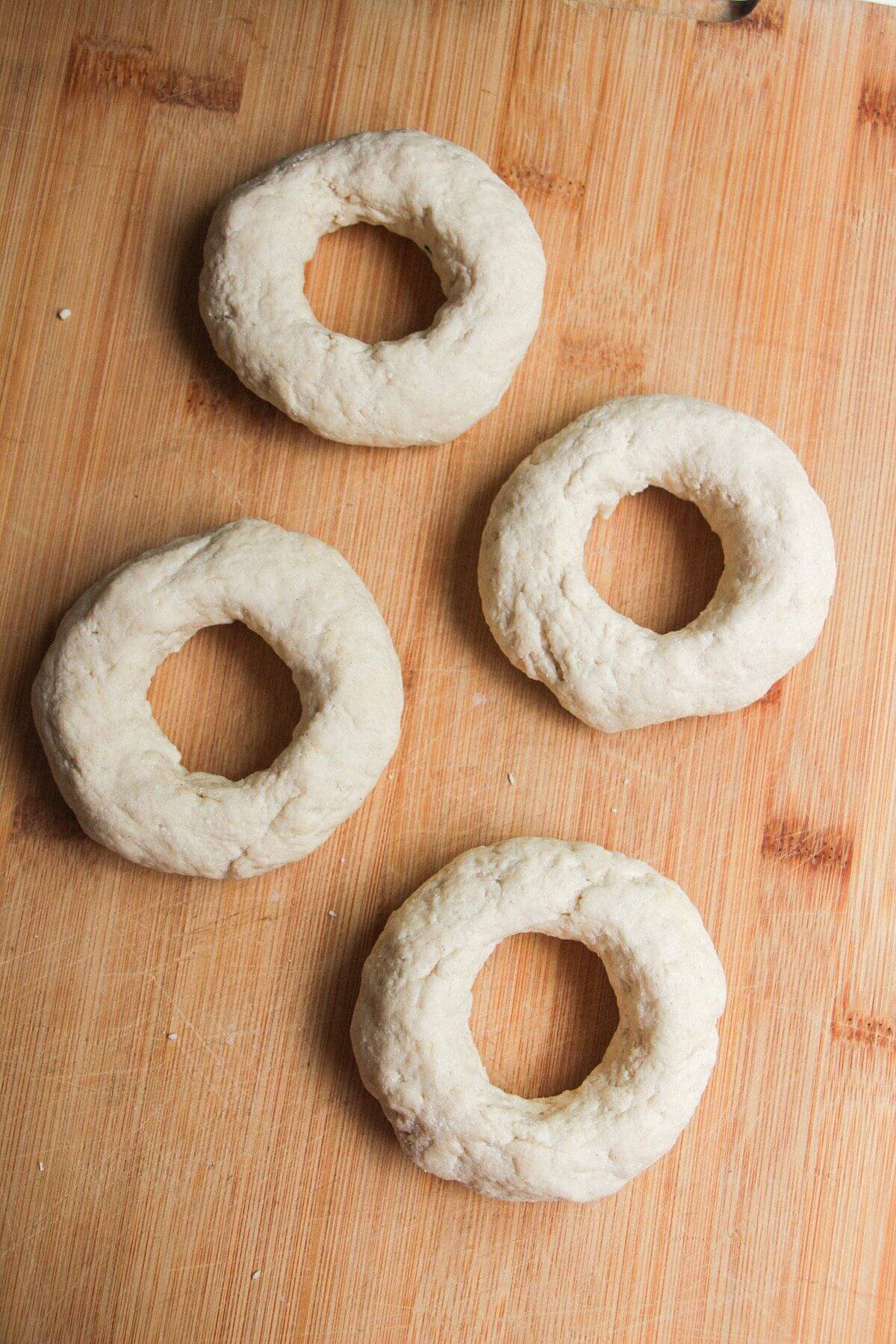 Four unbaked bagels on a wooden board.