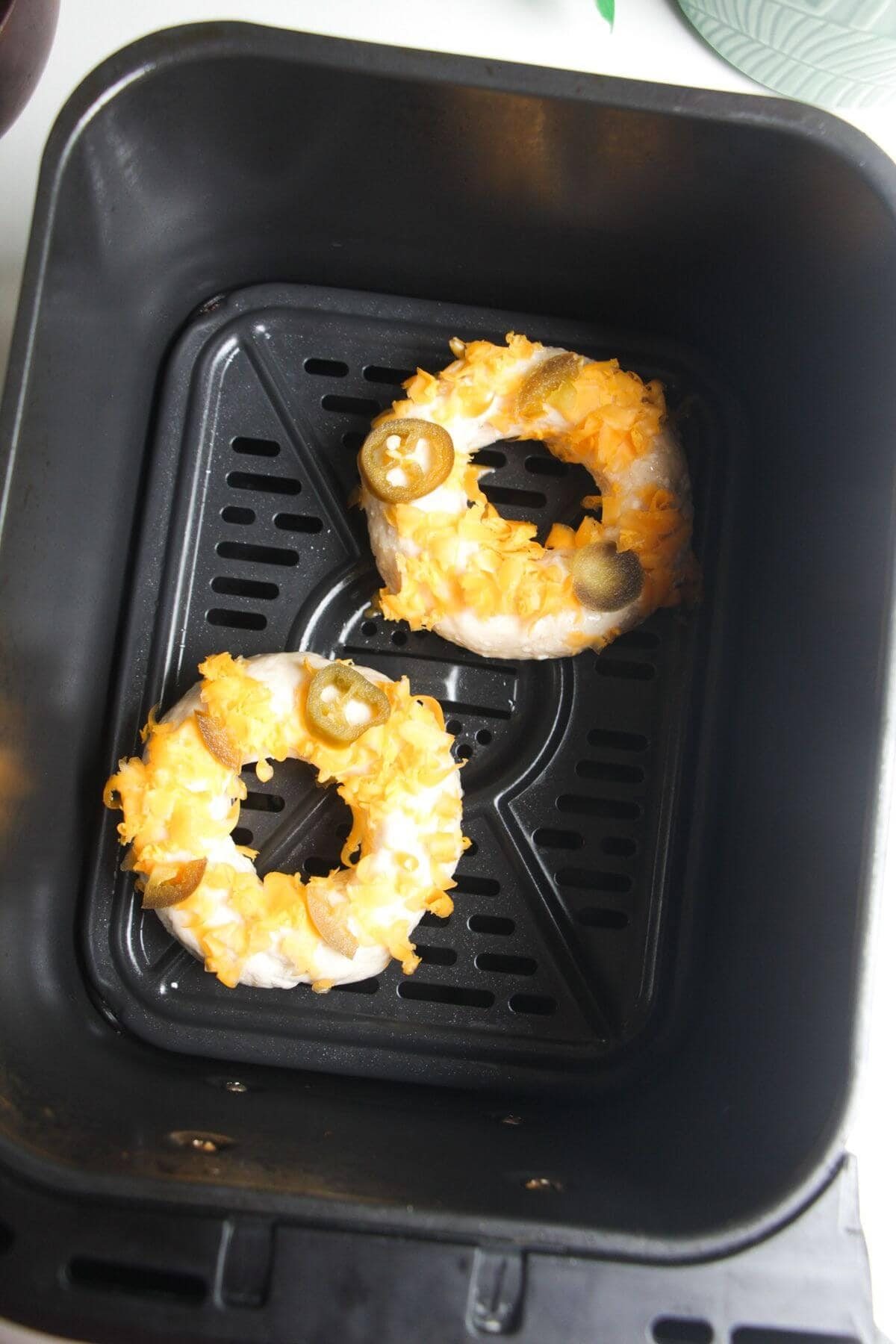 Two unbaked bagels in an air fryer basket.