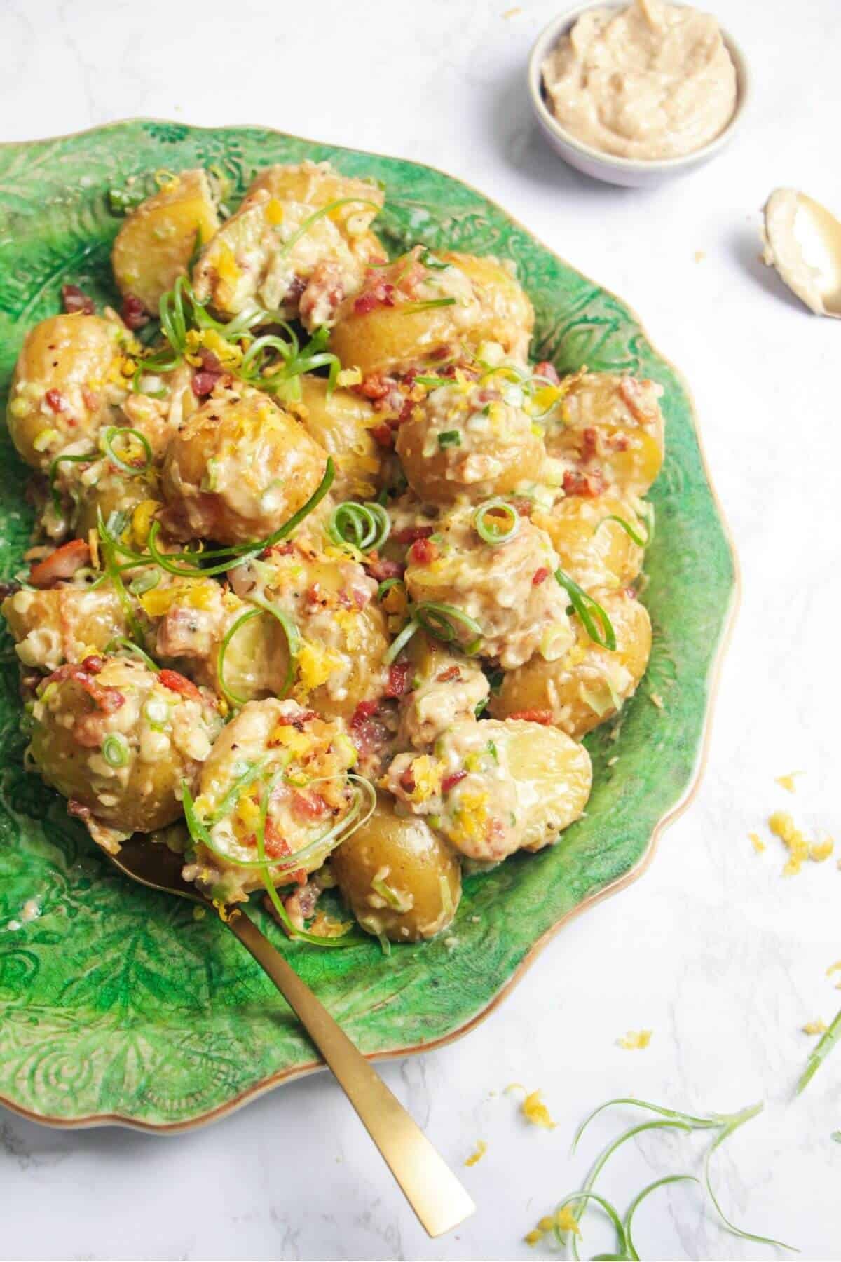 Close up of creamy Caesar potato salad on a large green serving plate with more Caesar dressing on the side.