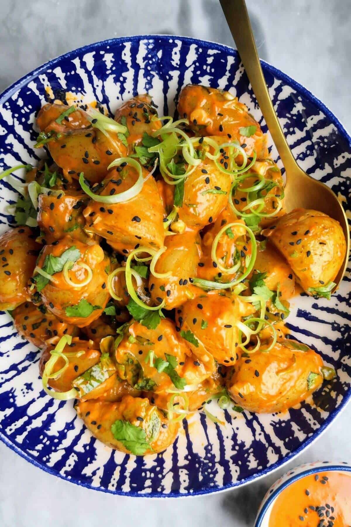 Orange gochujang potatoes in a white and blue bowl with small bowl of gochujang aioli on the side.