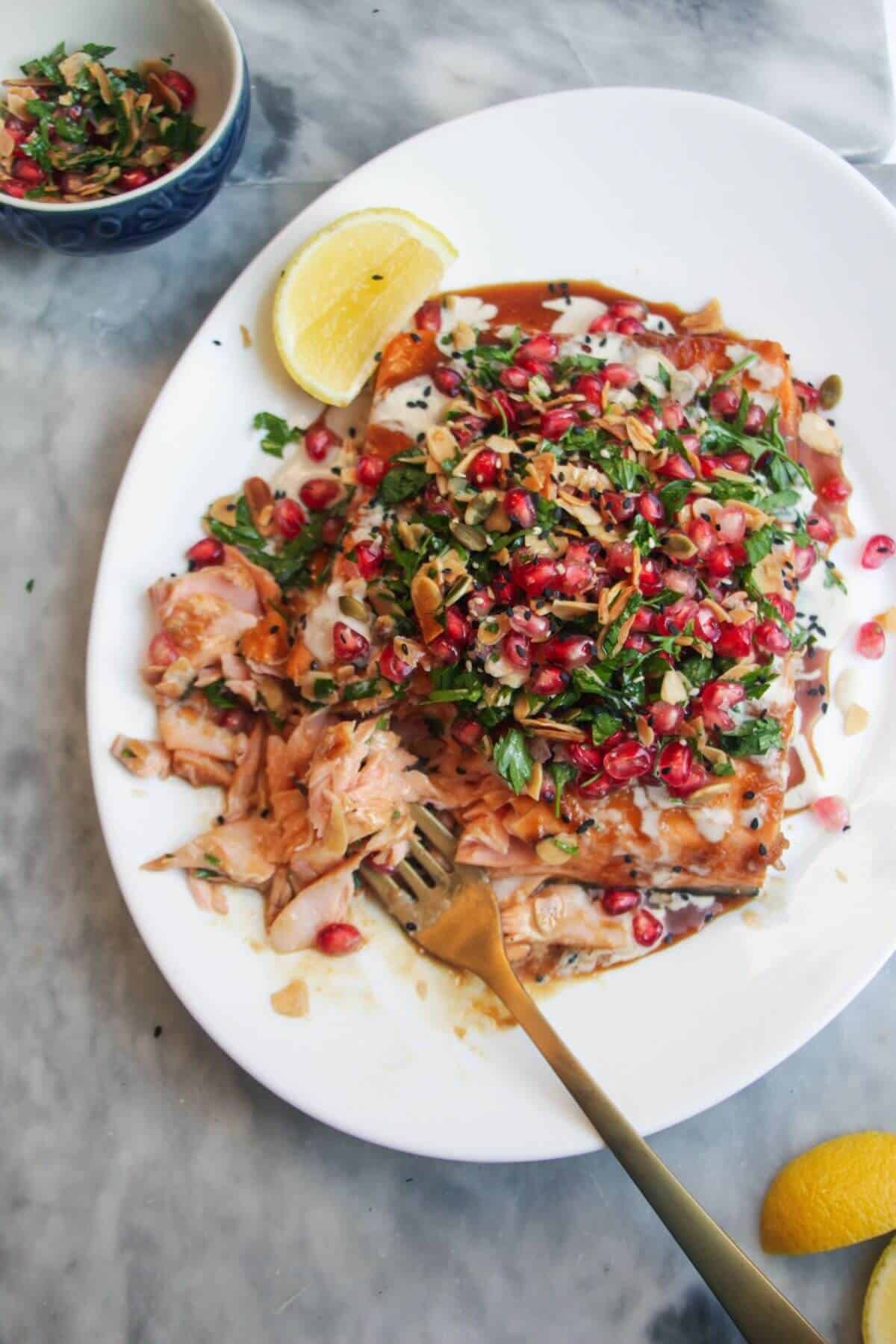 Maple miso glazed salmon fillet with pomegranate almond salsa, with lemon wedges on the side.