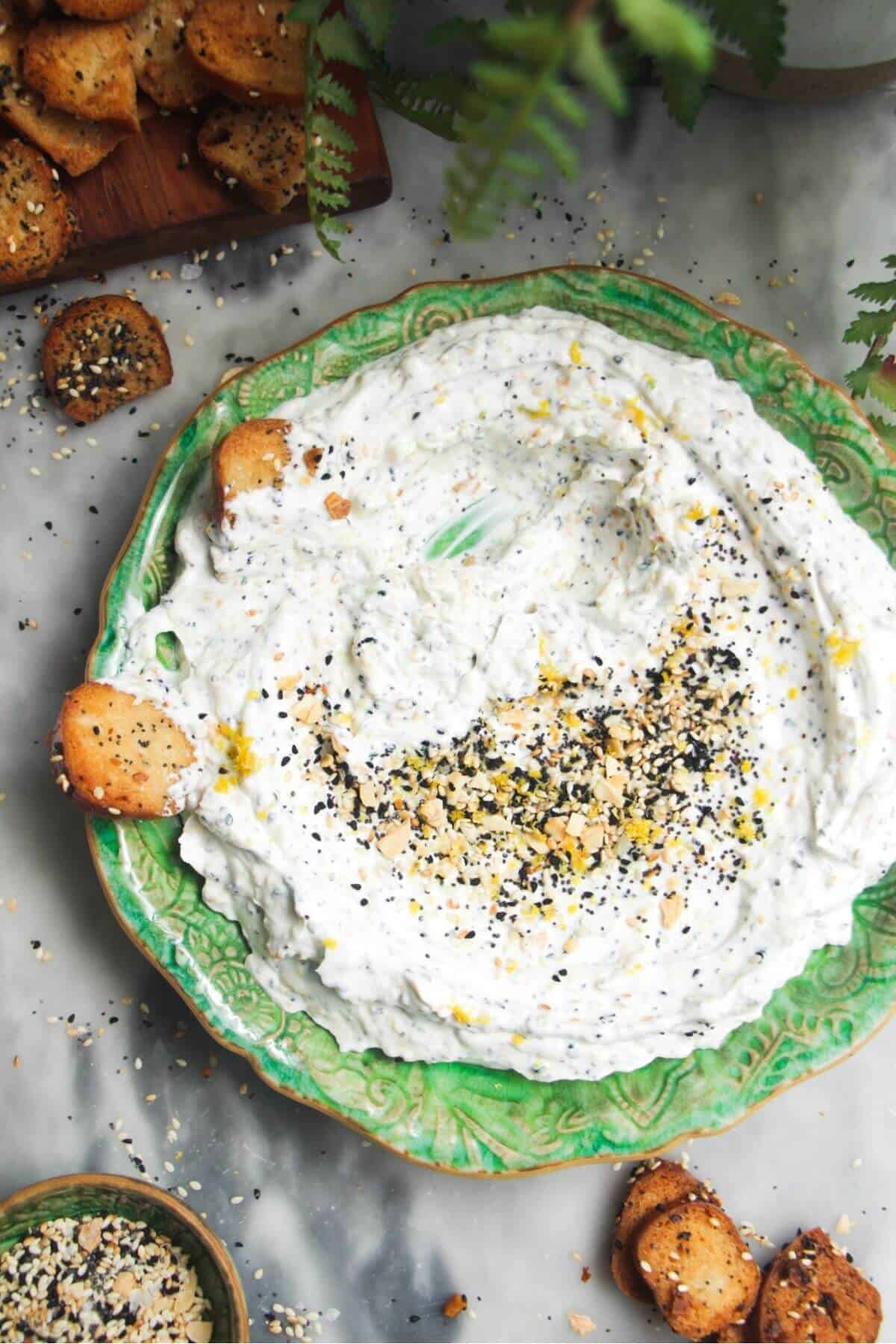 Everything bagel dip on a small green plate with bagel chips on the side.