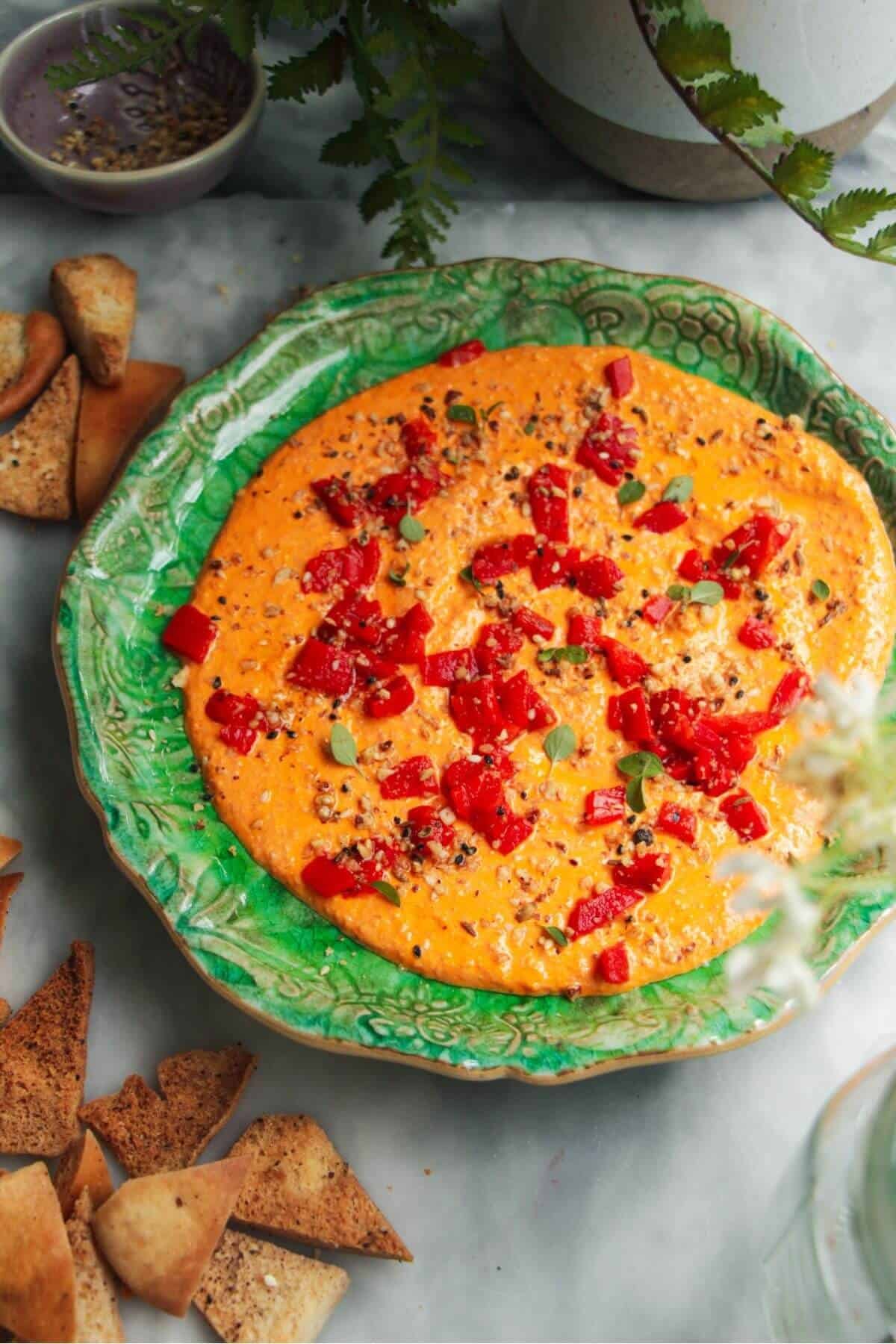 Red pepper feta dip on a small green plate with pita chips on the side.