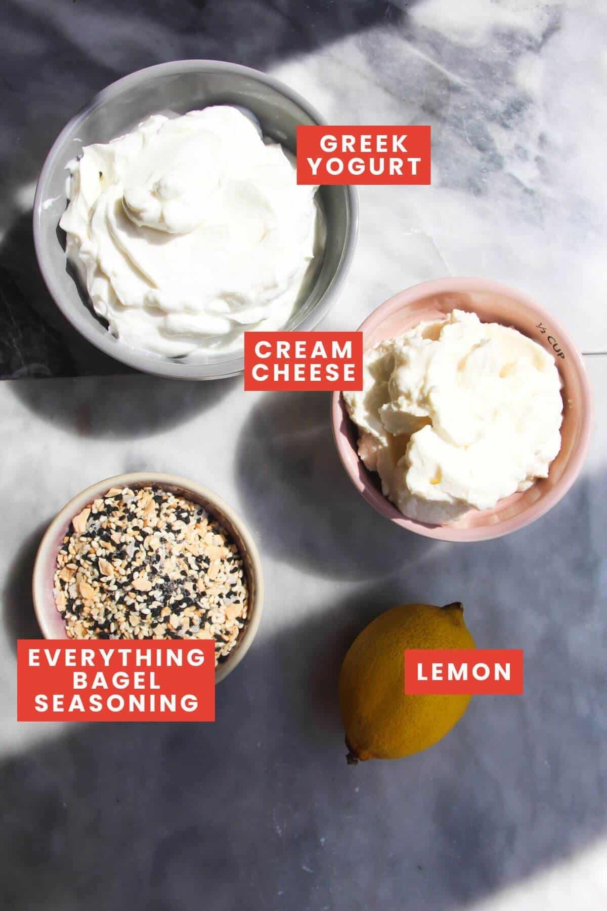 Ingredients for everything bagel dip on a grey marble background and labelled.