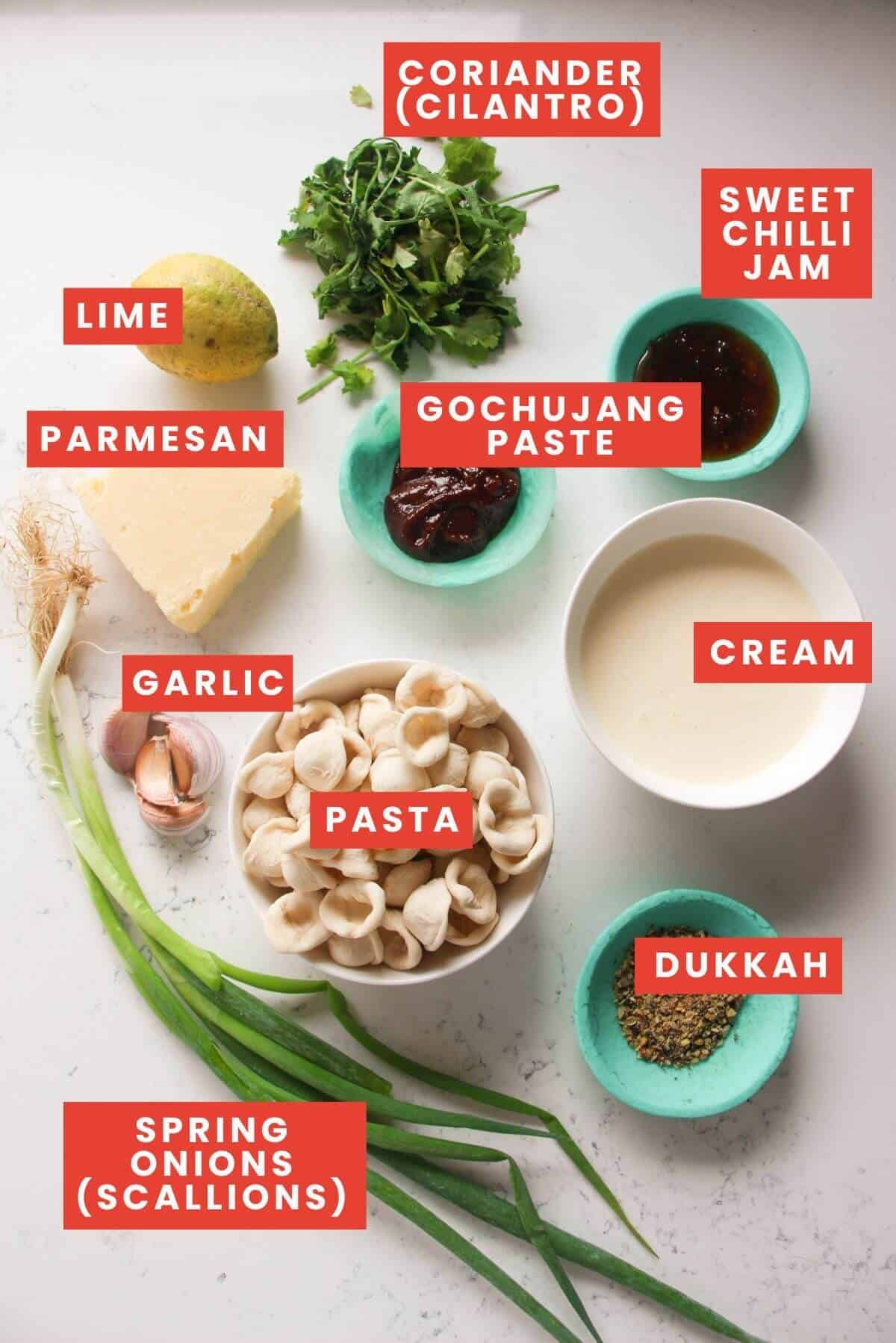 Ingredients for gochujang pasta laid out on a white marble background and labelled.