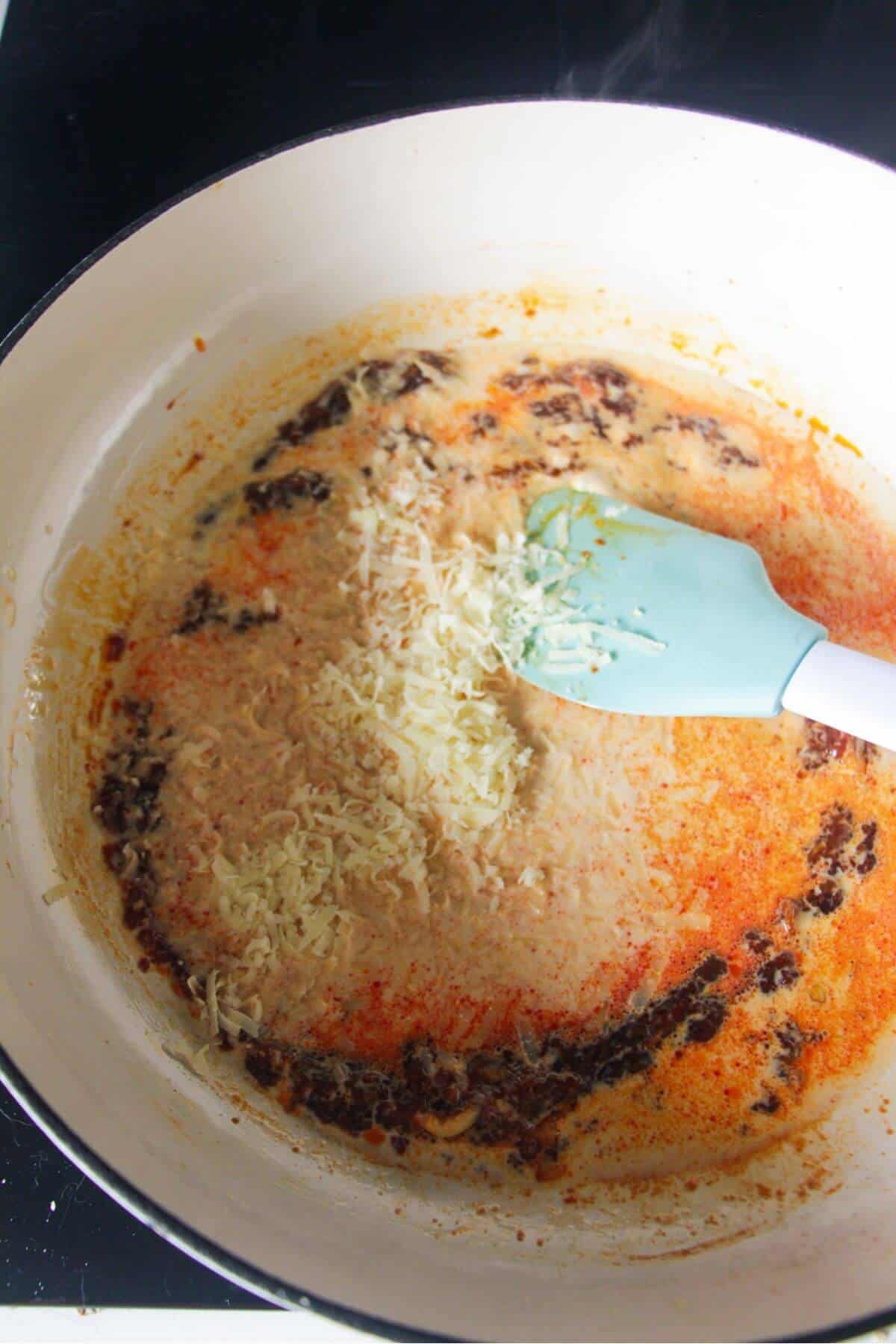 Parmesan and cream added to gochujang paste in a large white skillet.