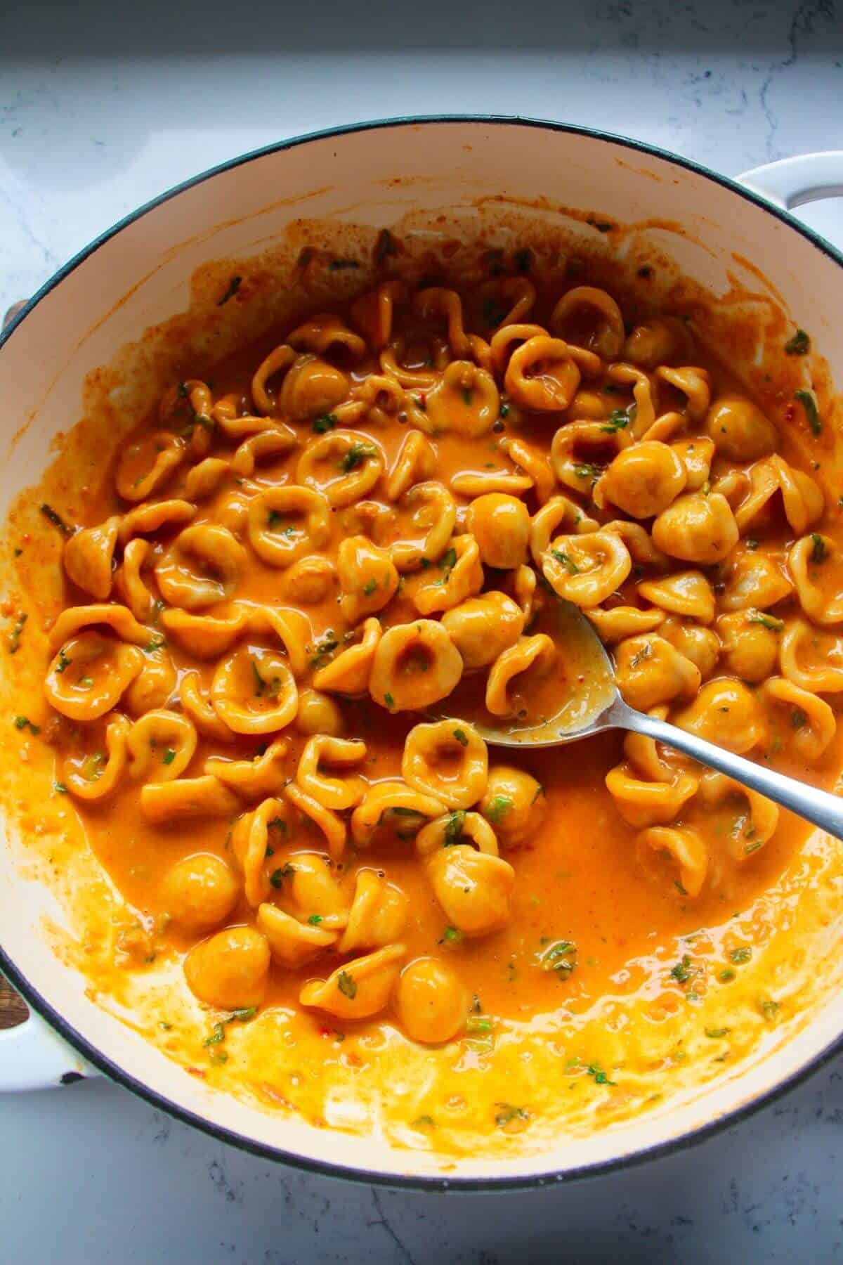 Gochujang pasta in a large white skillet, with a large silver serving spoon.