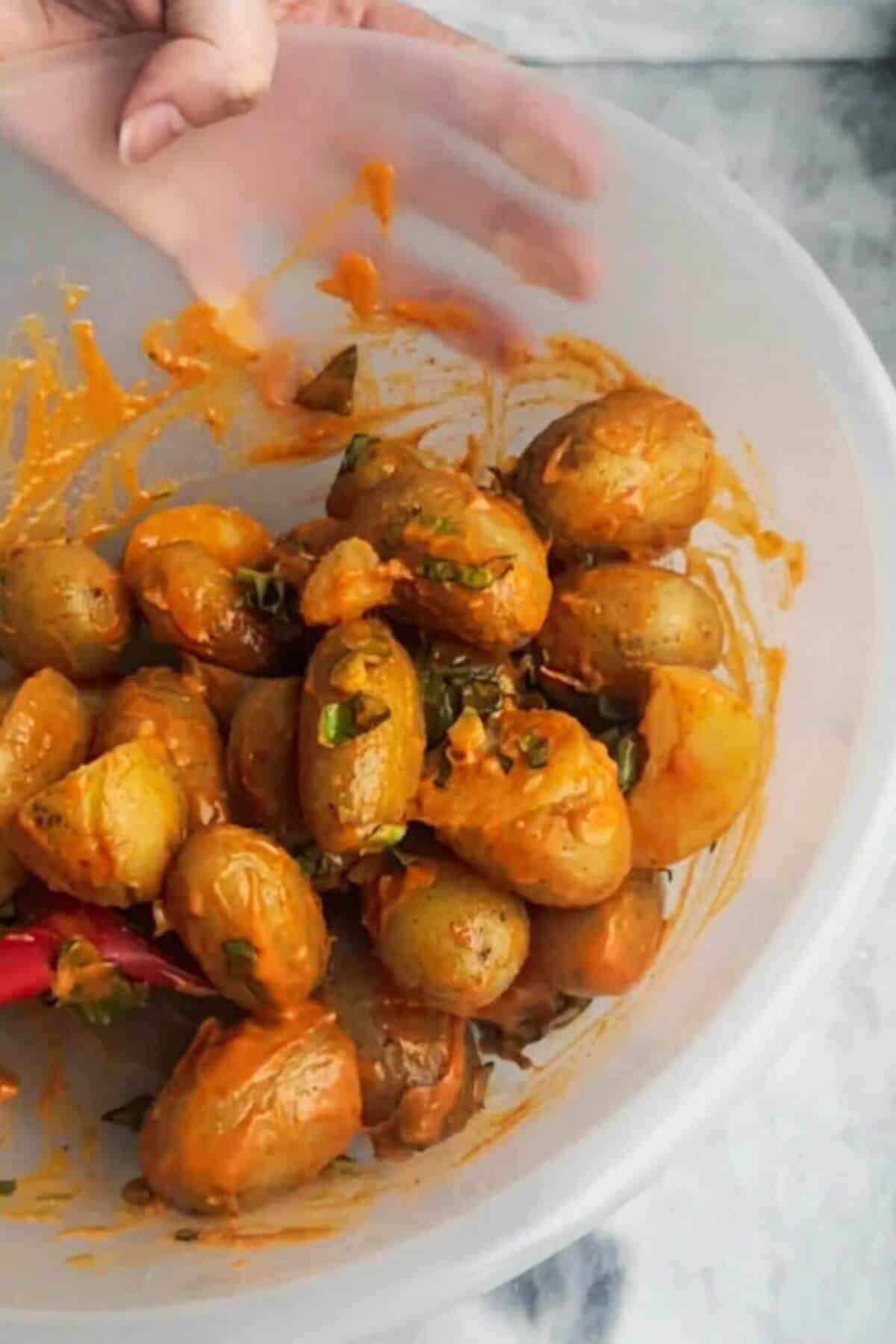 Hand holding large mixing bowl and mixing cooked potatoes and gochujang aioli together.