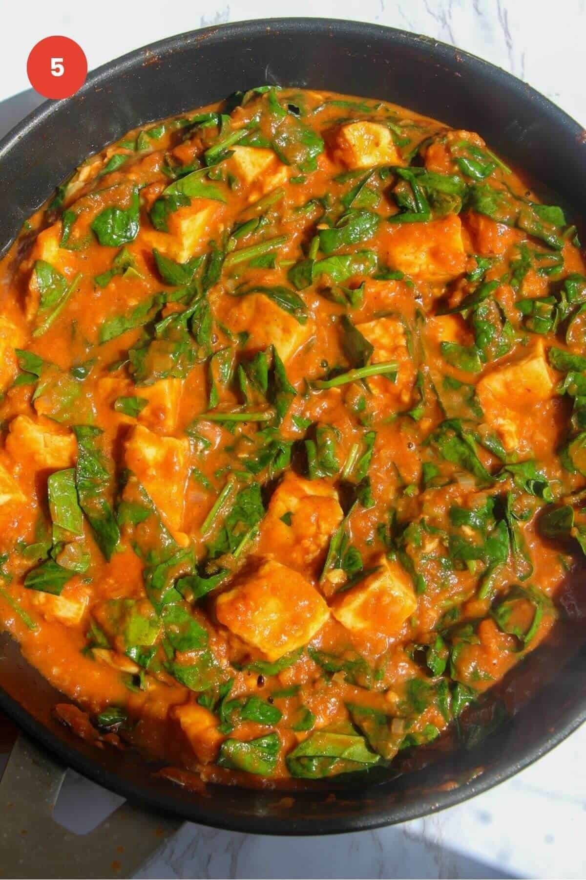 Spinach stirred through halloumi curry in a pan.