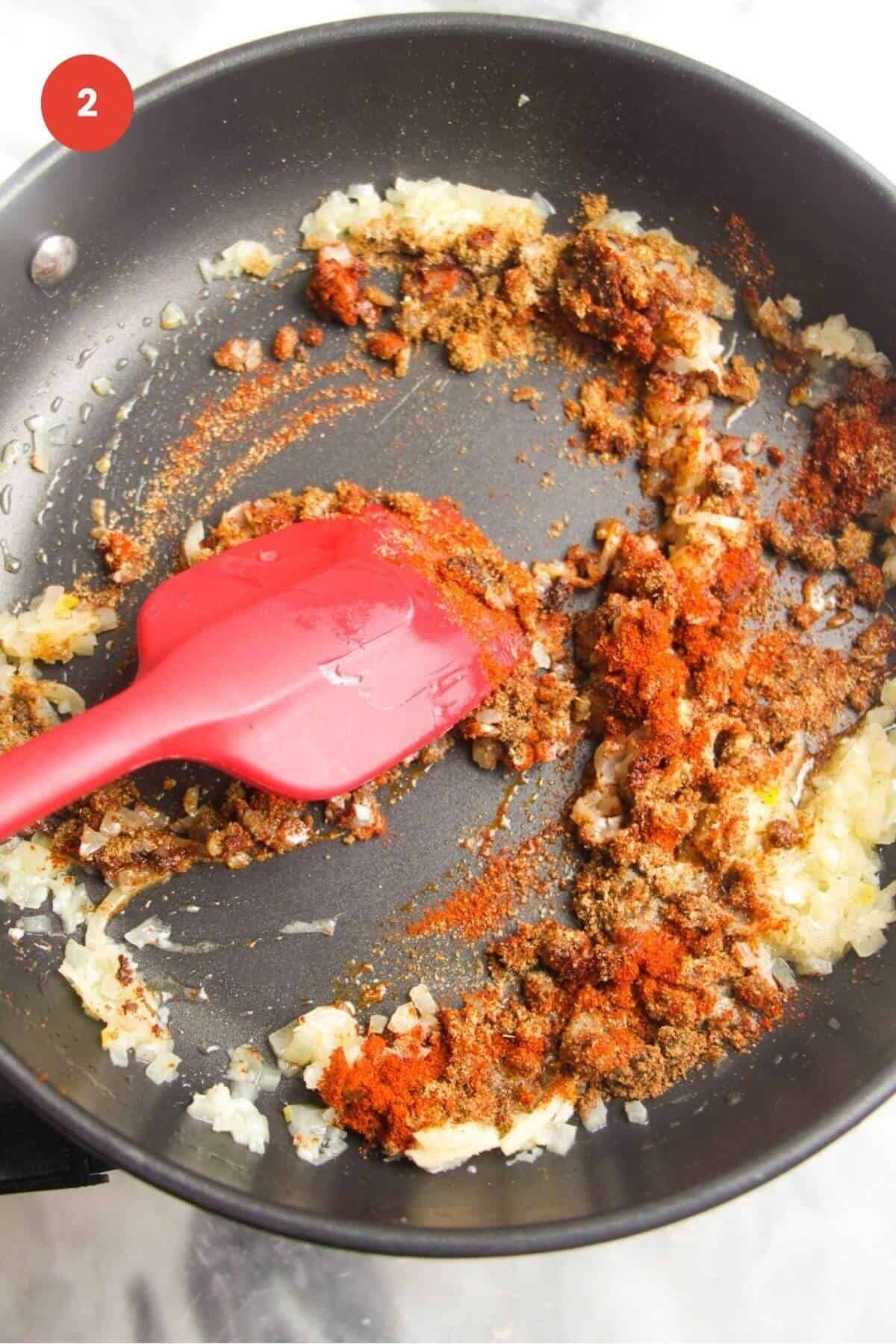 Spatula stirring spices and garlic in a pan.