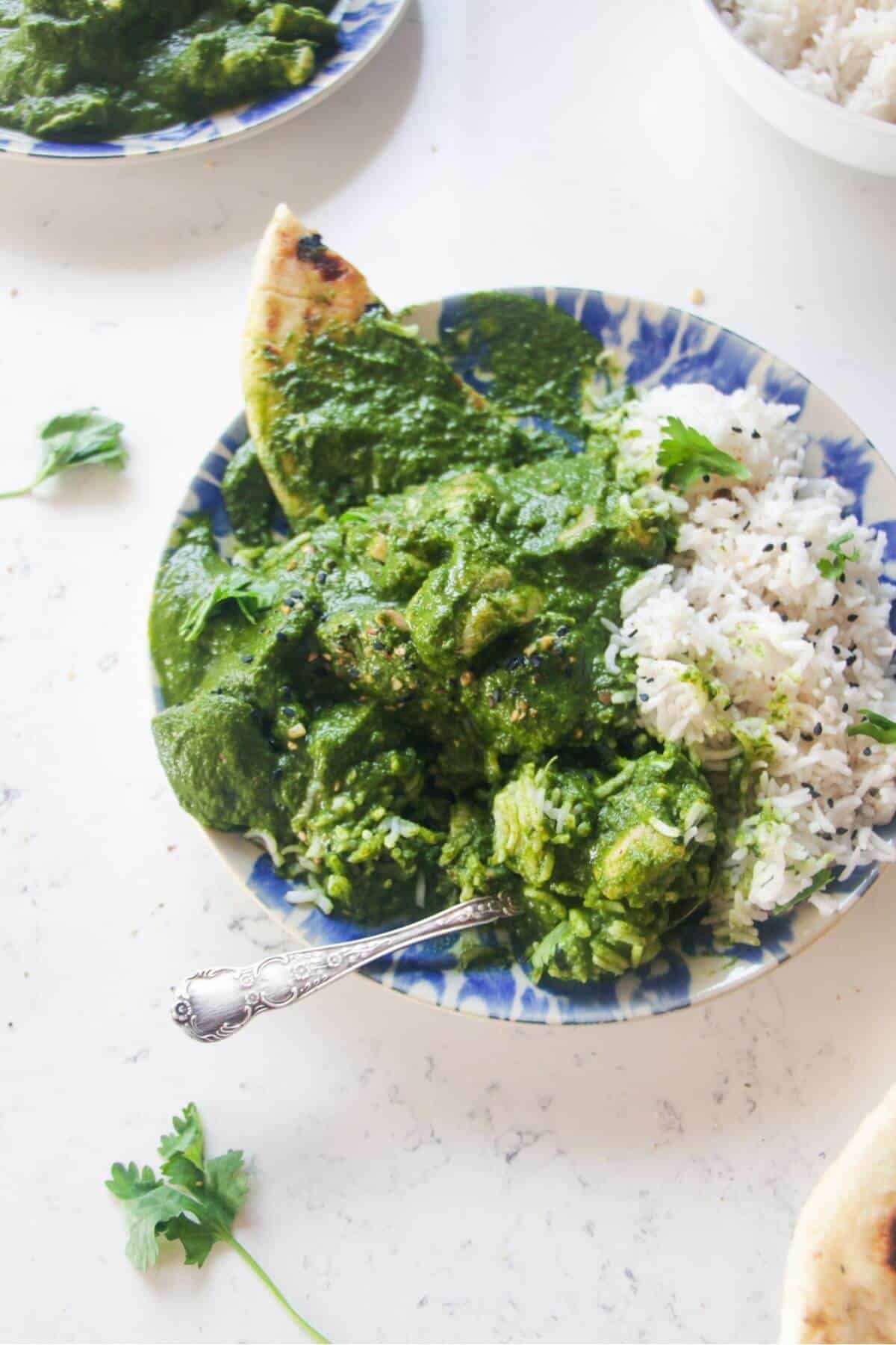 Chicken saag in with rice and naan on a white and blue plate.