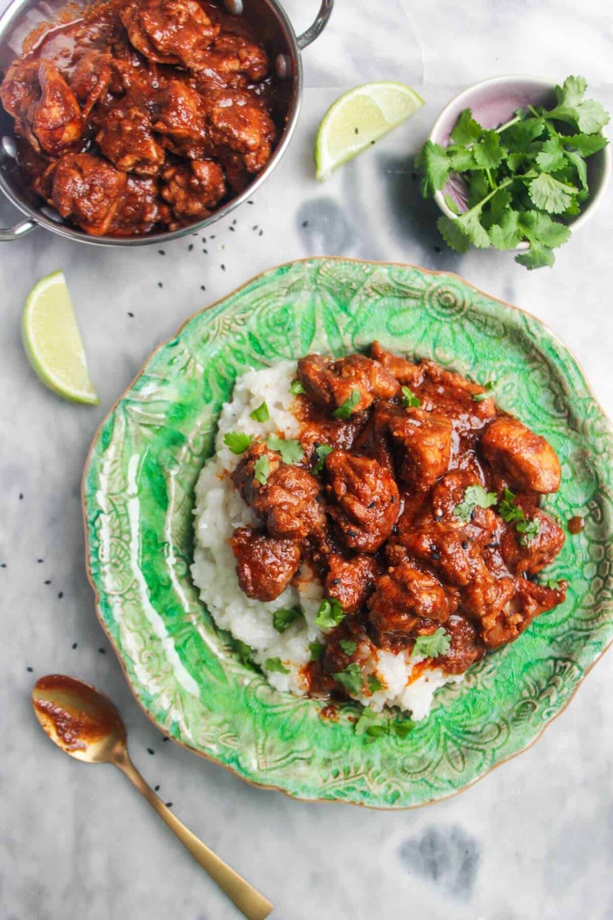 Chicken rogan josh on a bed of white rice on a green plate, with more curry in a small silver dish on the side.