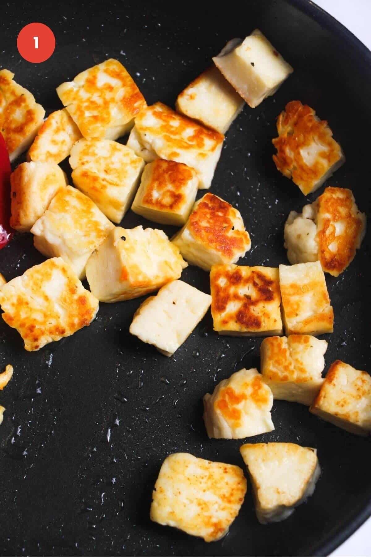 Halloumi cubes pan-frying in a pan.
