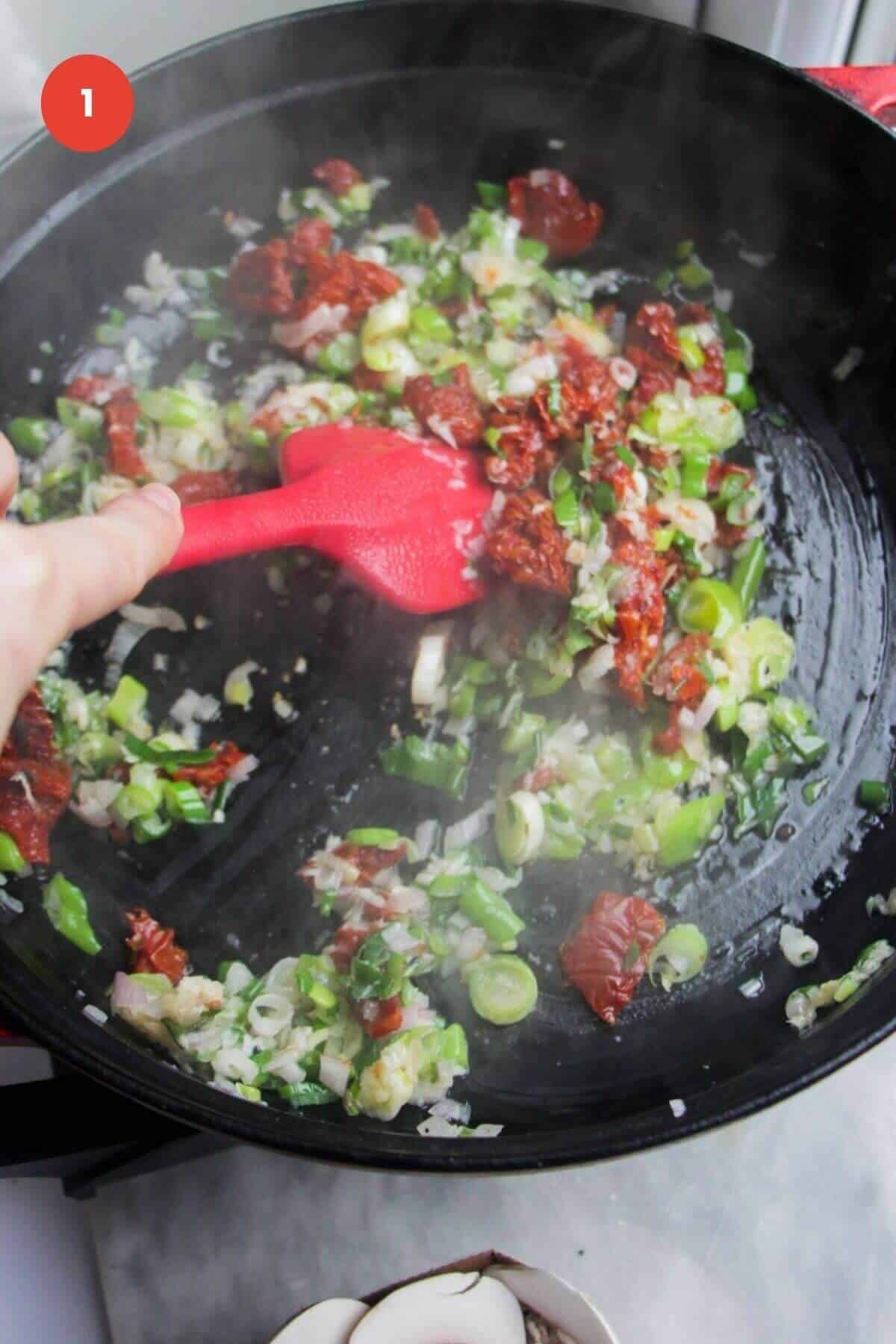 Sundried tomatoes and scallions cooking a large pan.