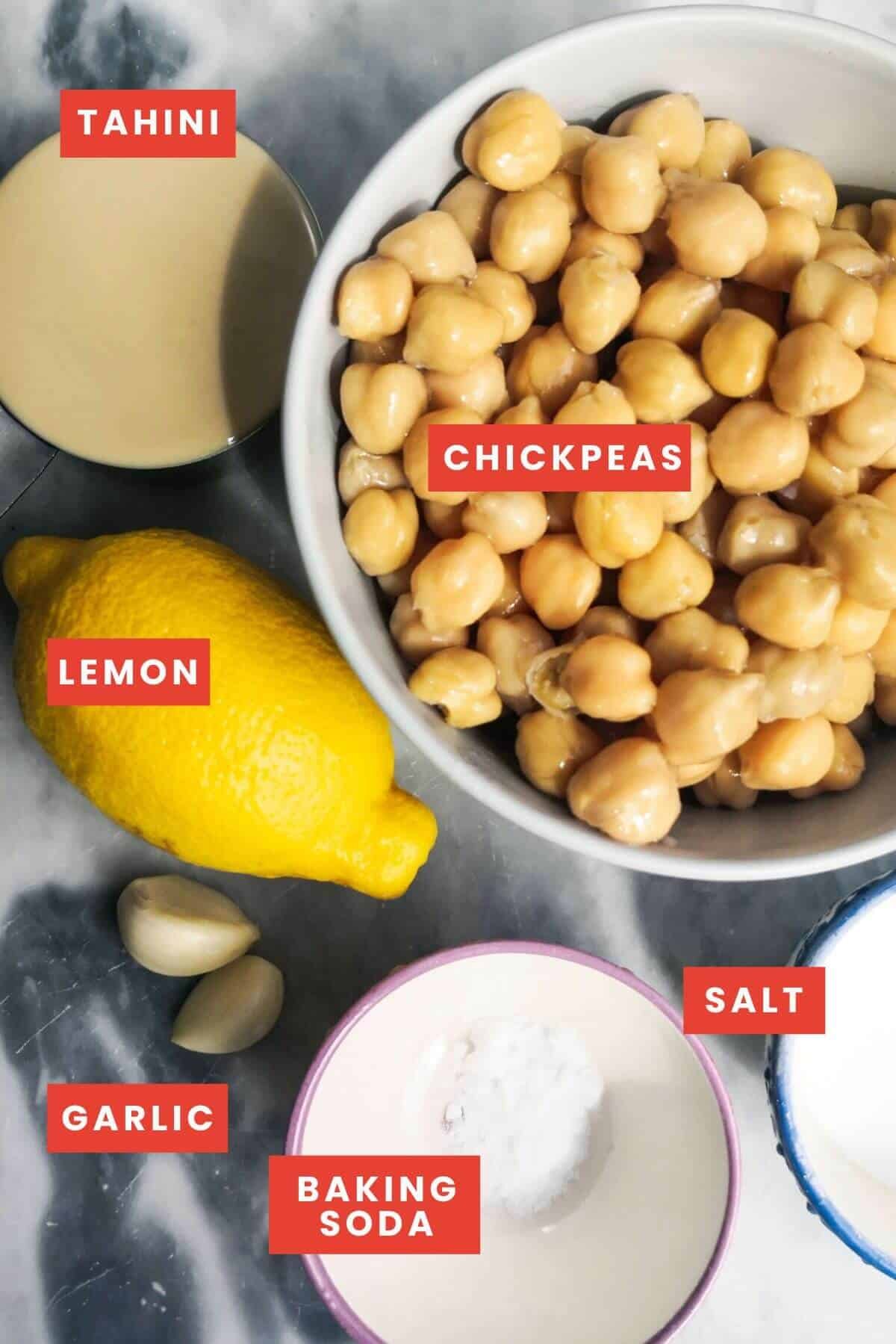 Ingredients for hummus laid out on a grey marble background and labelled.