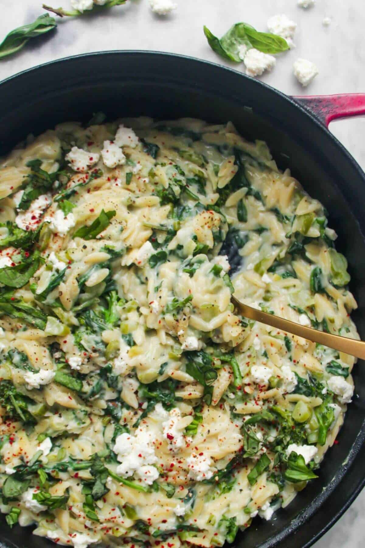 Creamy spinach and feta one pot orzo in a black and red pan on a grey marble background.
