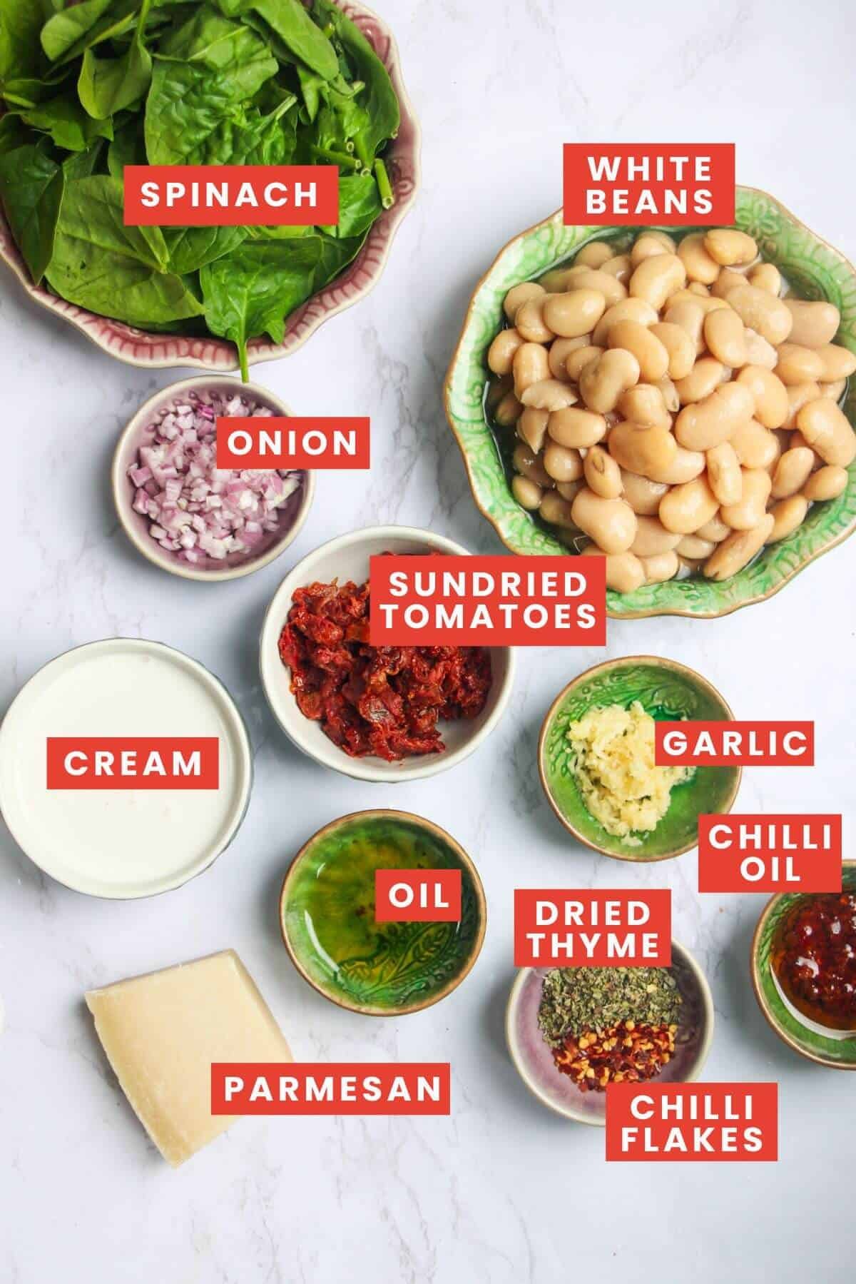Ingredients for creamy parmesan sundried tomato white beans on a white marble background and labelled.