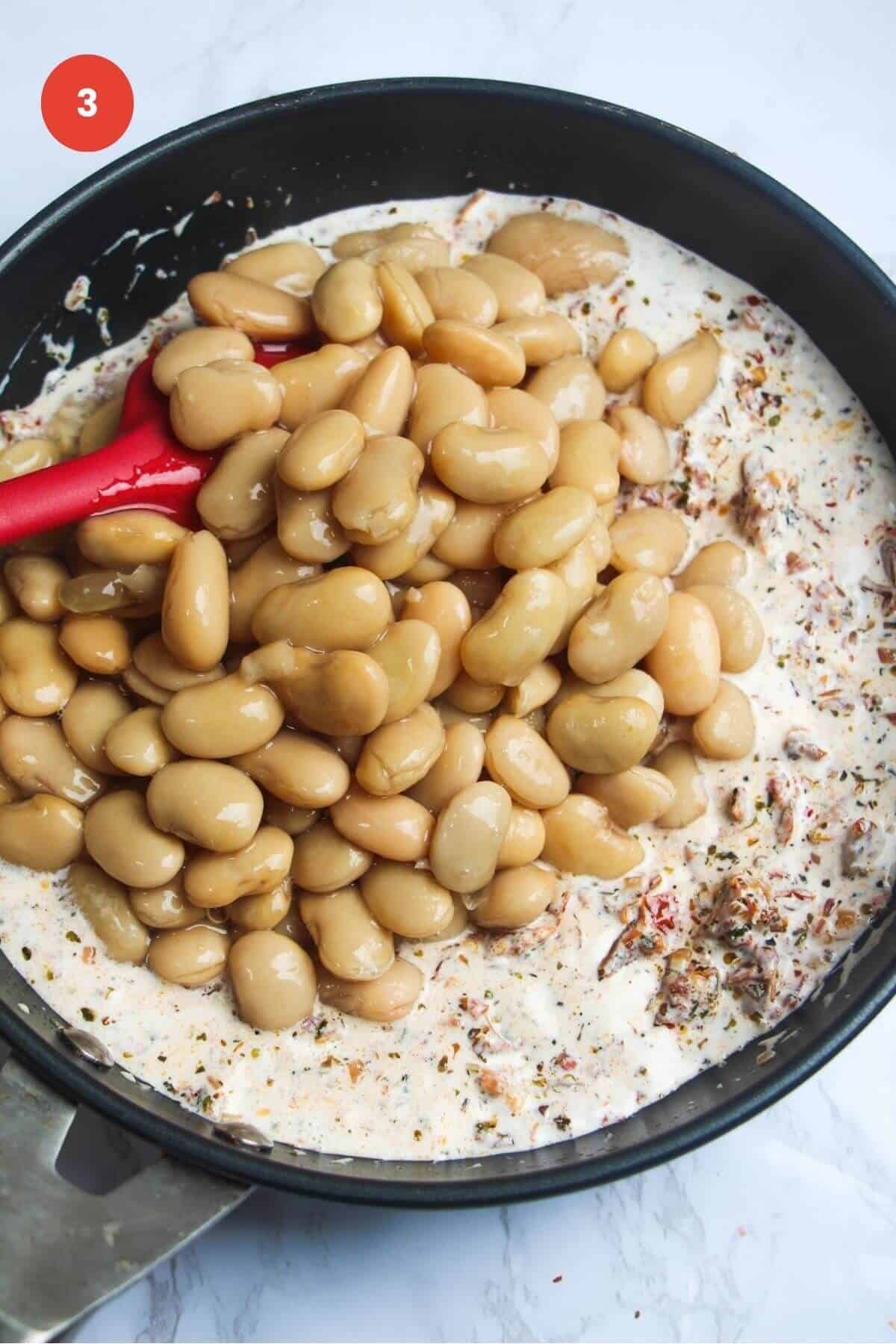 White beans added to creamy sauce in a skillet.