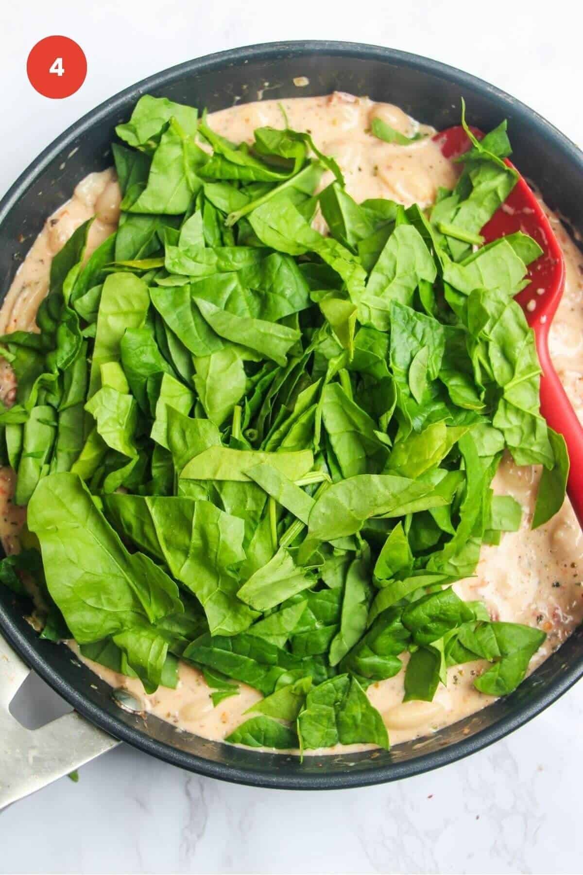 Spinach leaves added to creamy beans in a skillet.