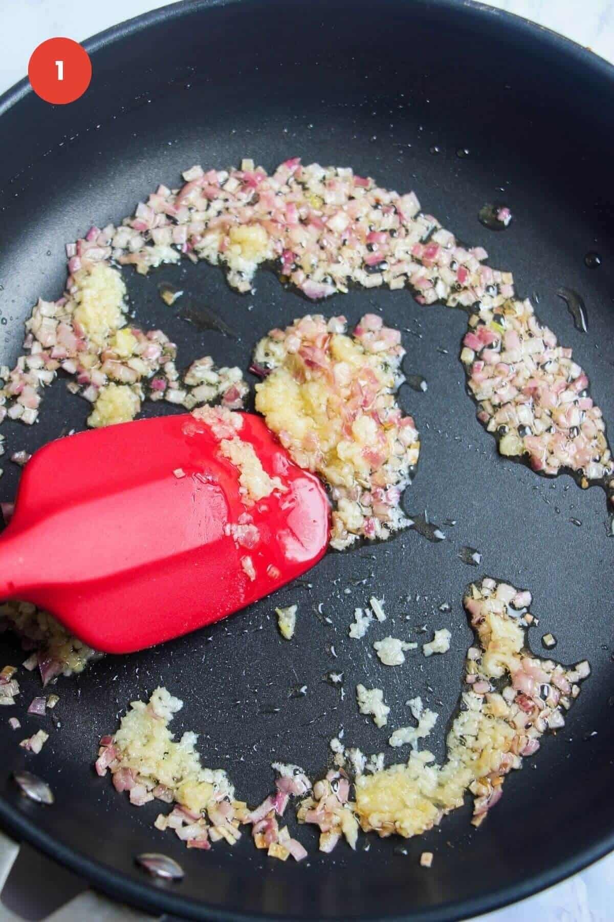 Spatula stirring onion and garlic in a skillet.
