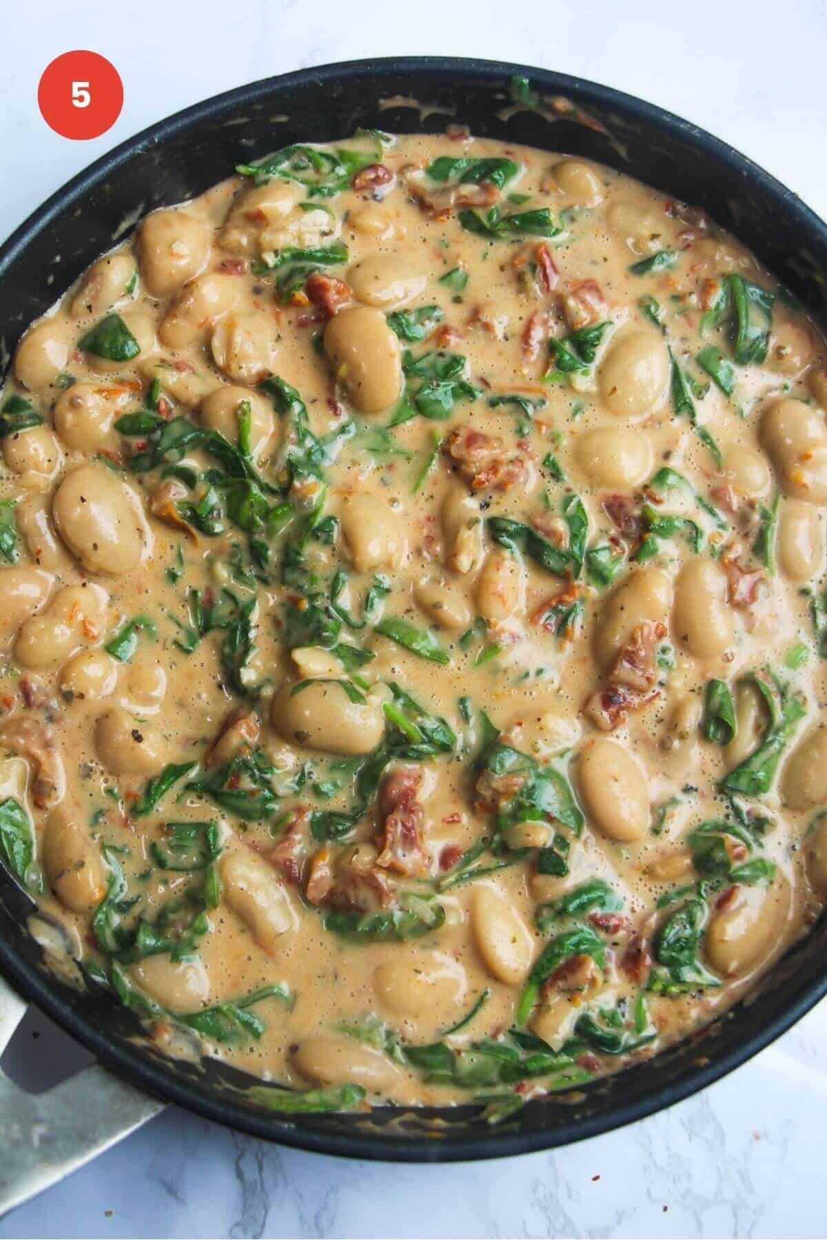 Spinach wilted into creamy beans in a skillet.