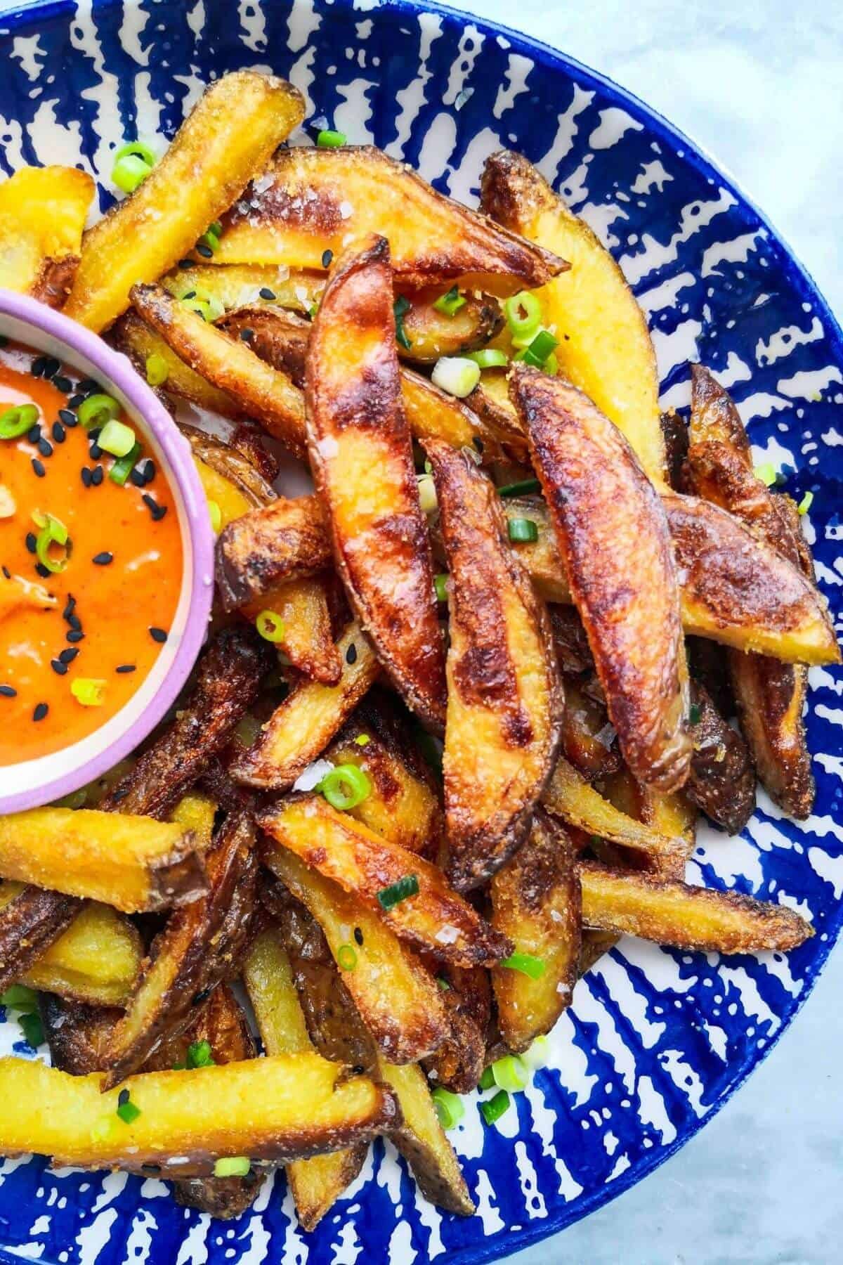 Homemade oven chips with spicy gochujang aioli in a white and blue striped bowl.