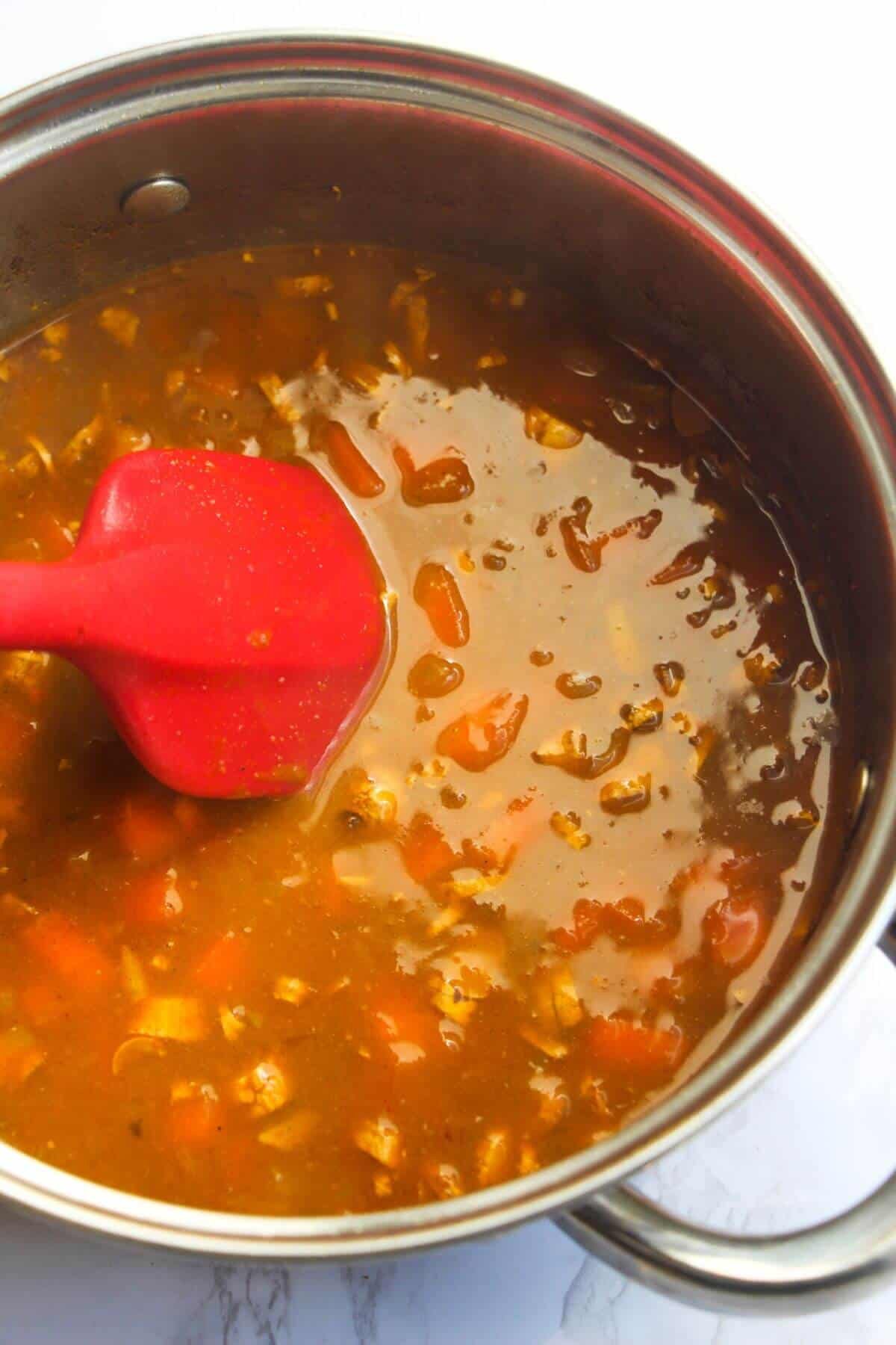 Red spatula stirring reduced katsu sauce in a small silver pot.