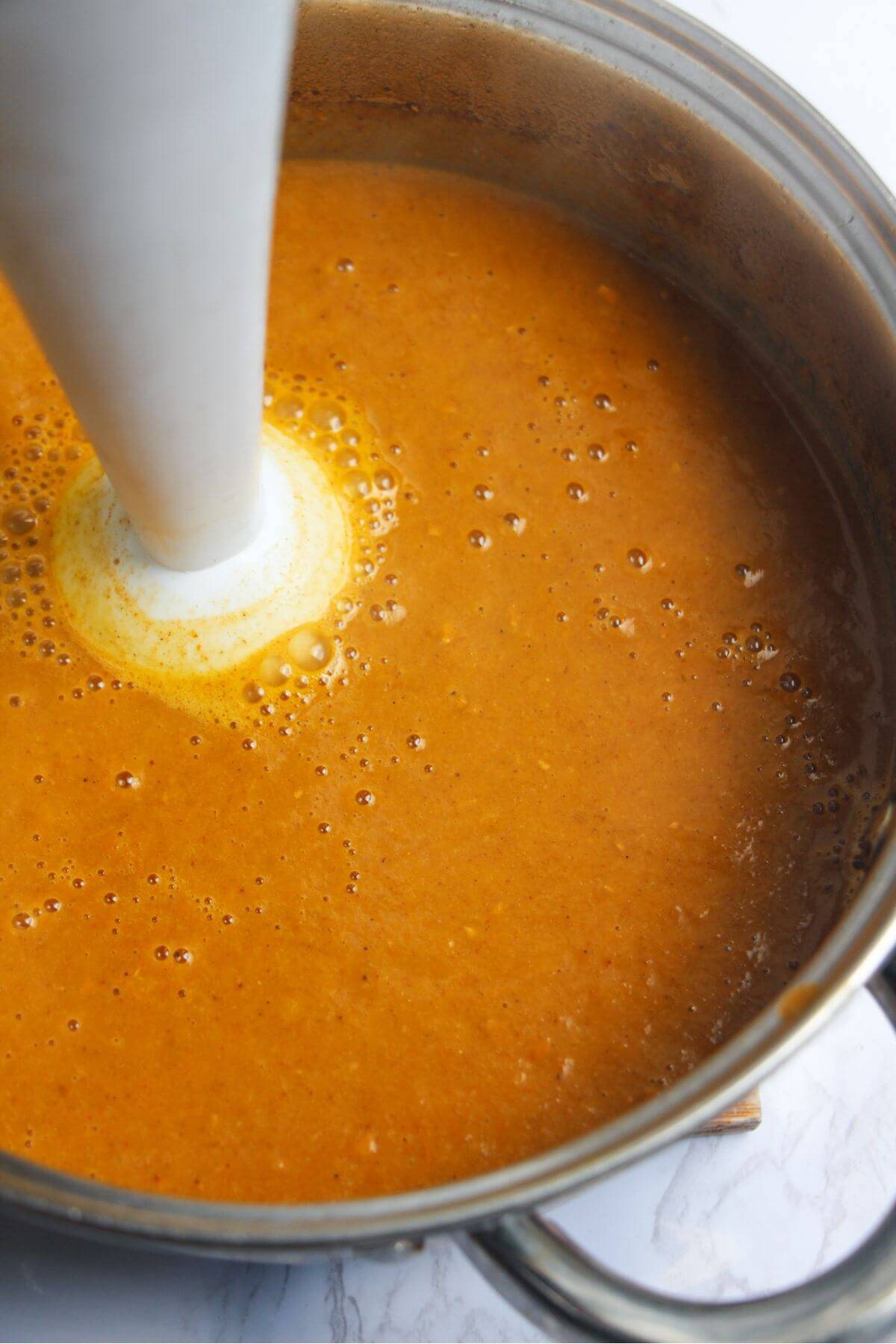 White stick blender in a small silver pot, blitzing the katsu sauce smooth.