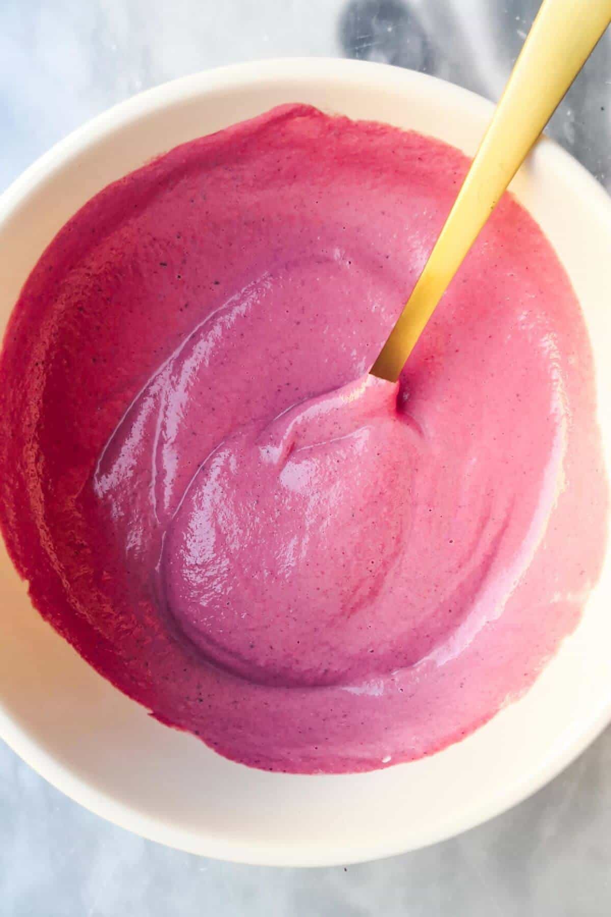 Bright pink beetroot tahini sauce in a small white bowl with a gold spoon in it.