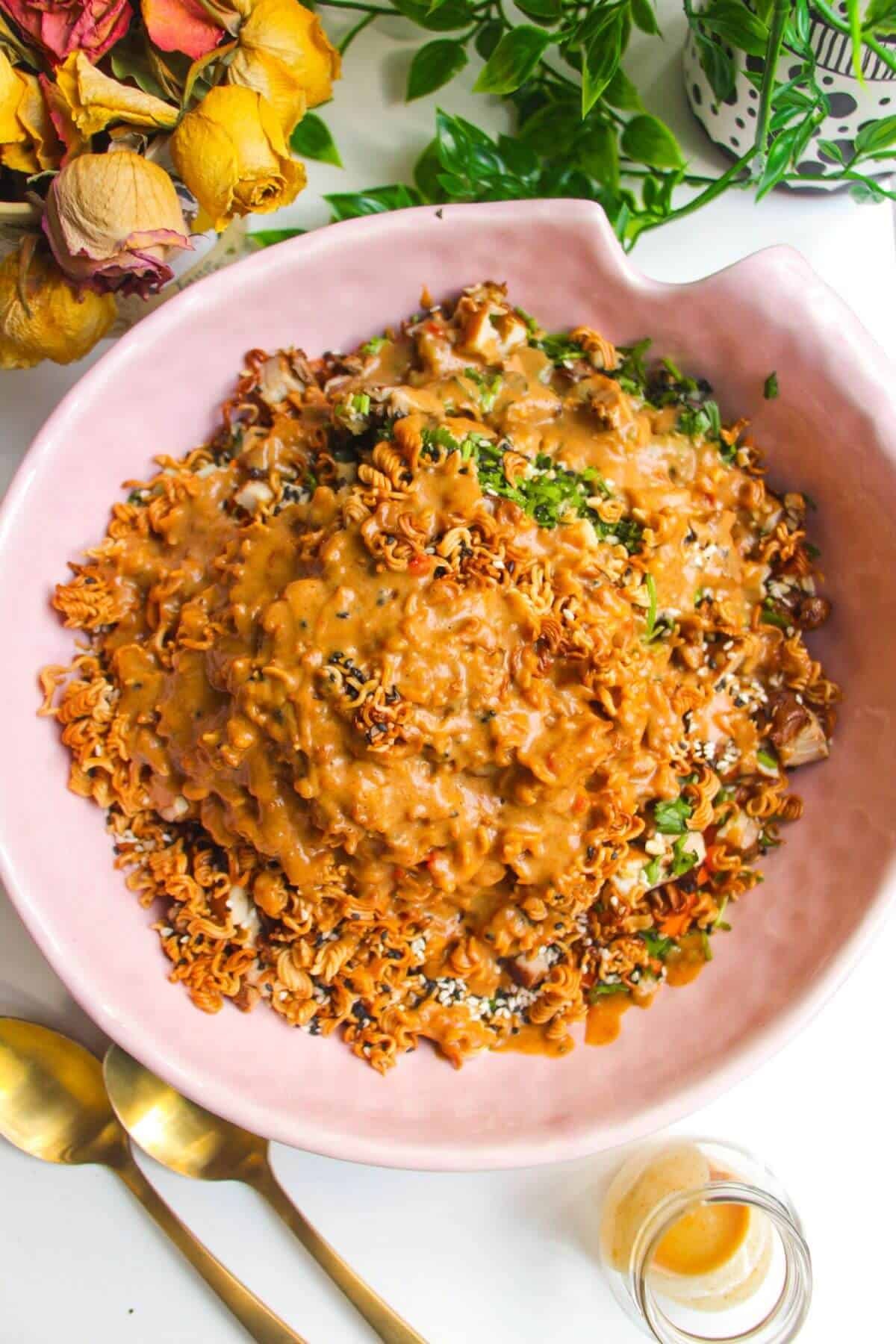 Peanut satay dressing poured over crispy ramen salad in pink bowl.