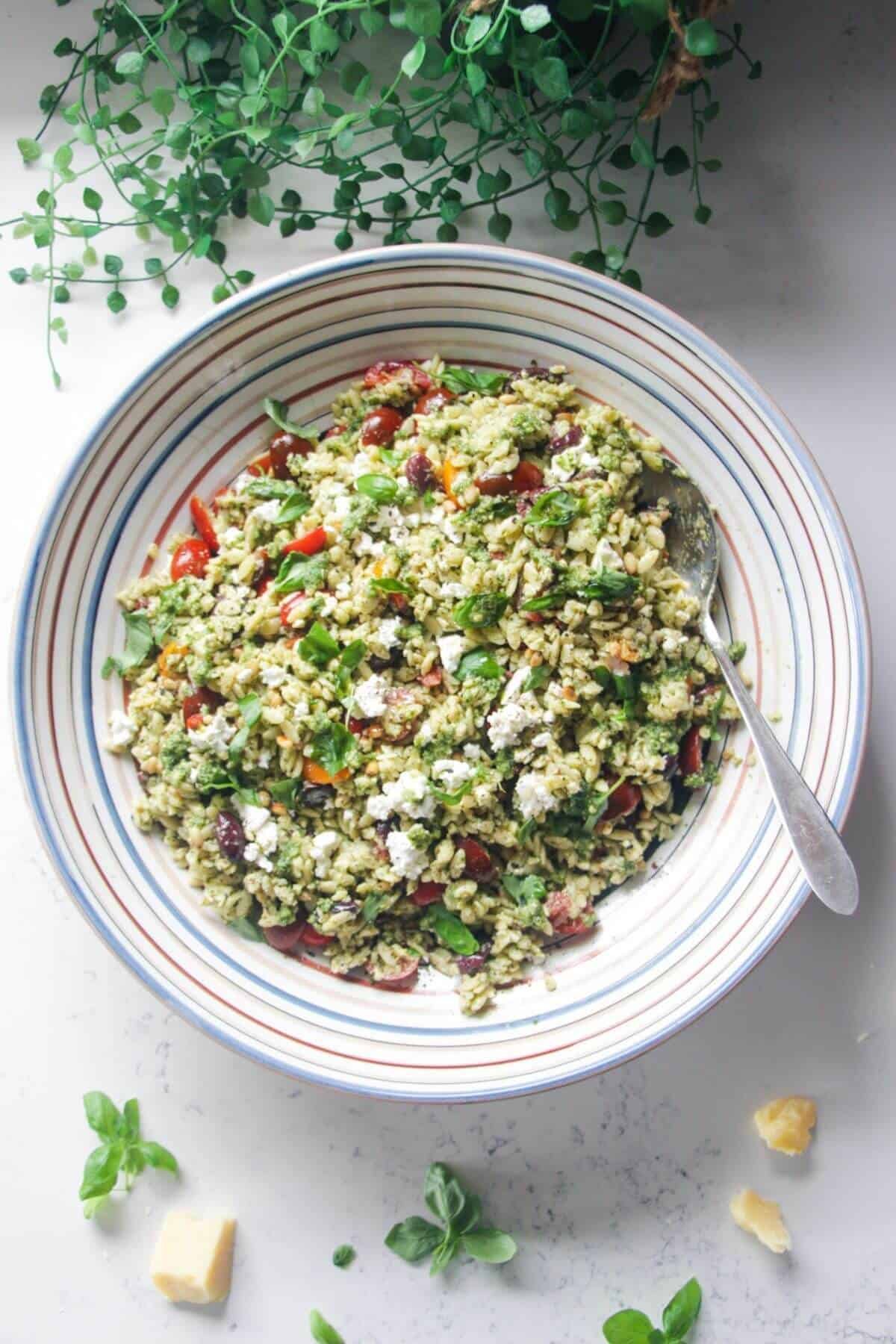 Orzo pesto salad in a large colourful serving bowl with a silver spoon.