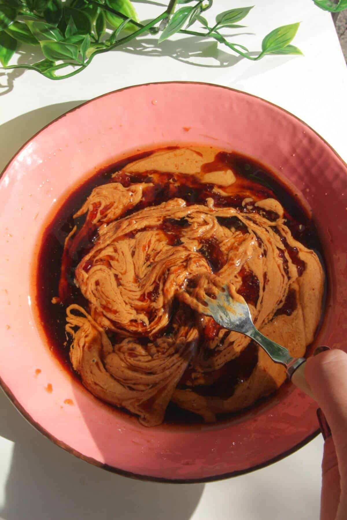 Mixing peanut butter with soy sauce and other ingredients in a bowl.