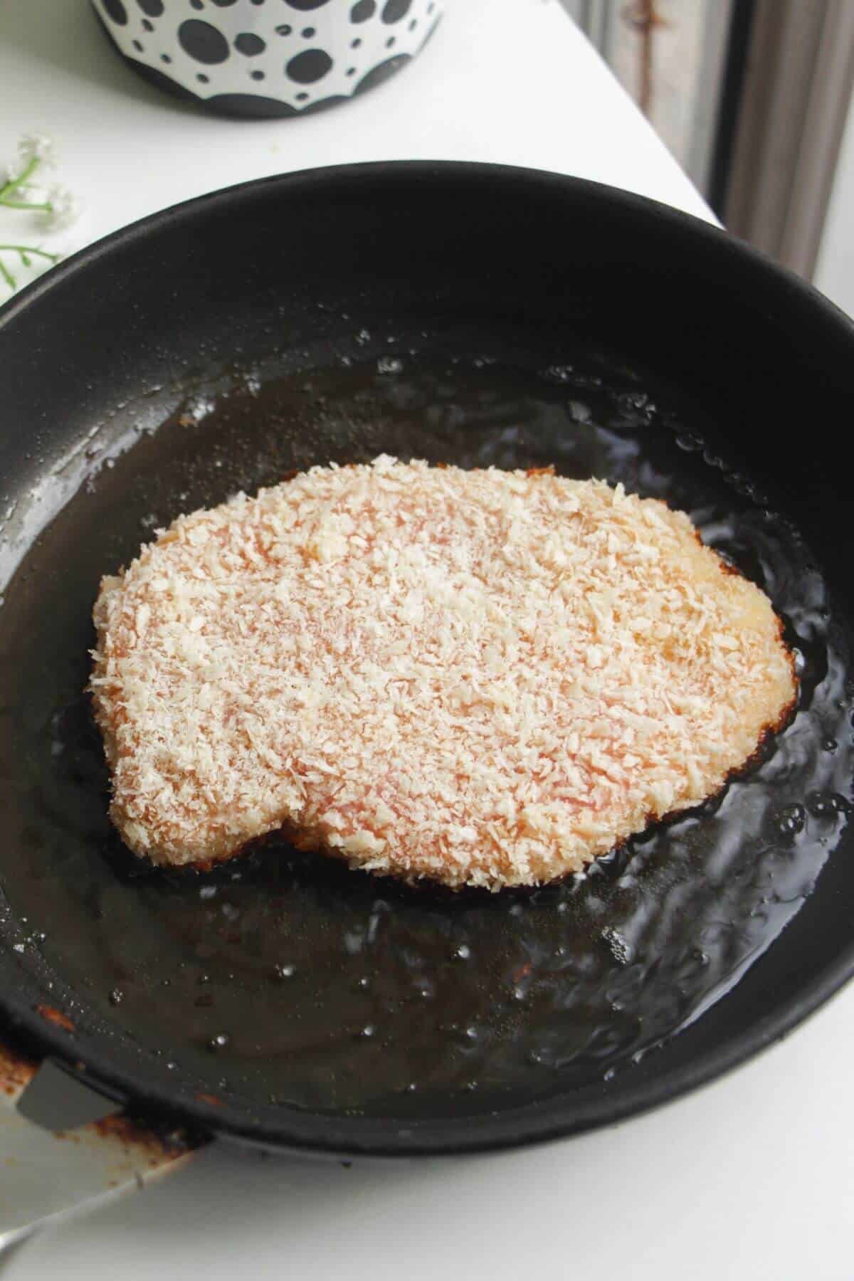 Breaded chicken breast in a small pan.