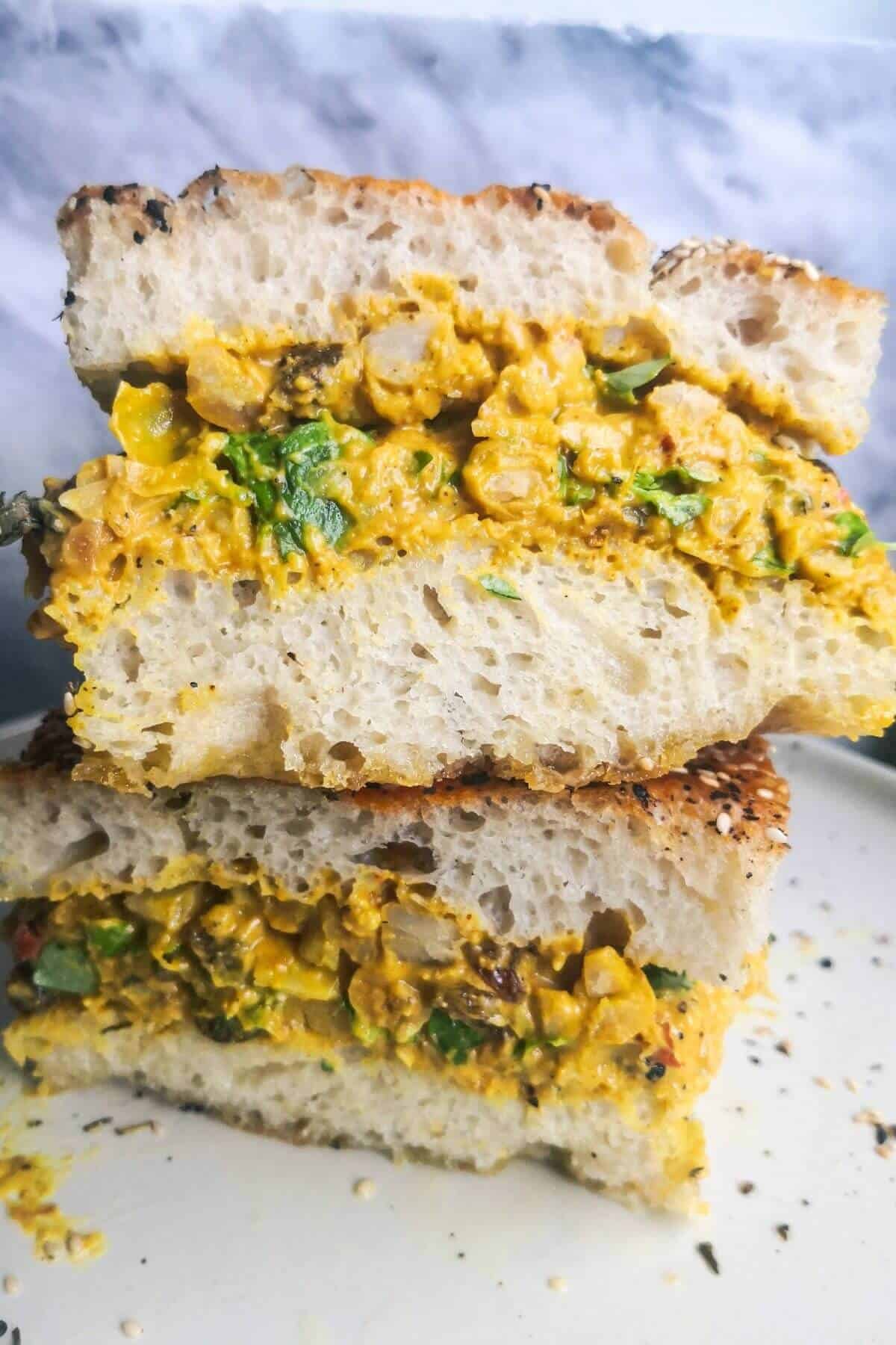 Two coronation chickpea stuffed focaccia sandwiches on top of each other on a white plate.