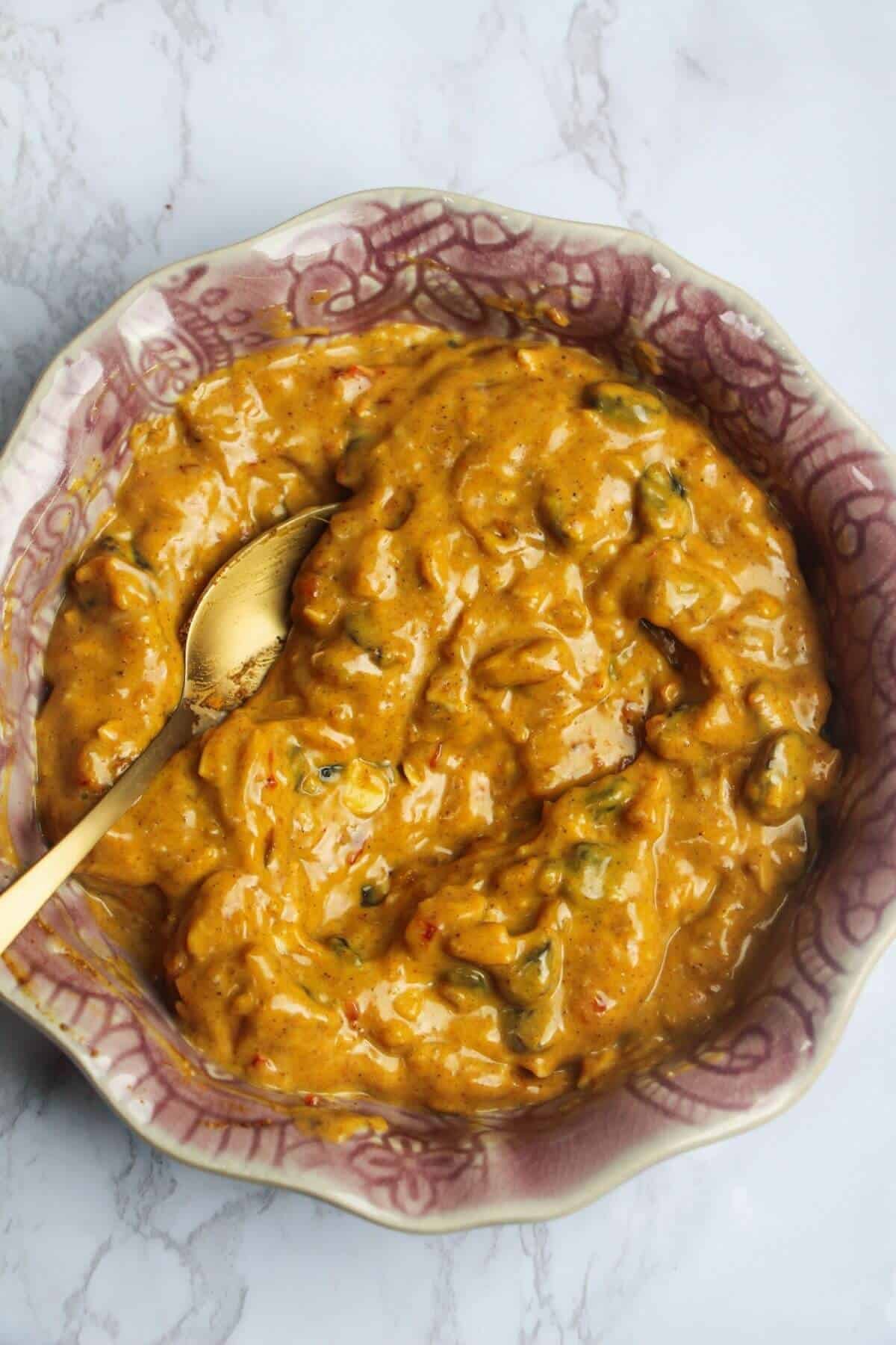 Coronation sauce mixed with a spoon in a small pink bowl.