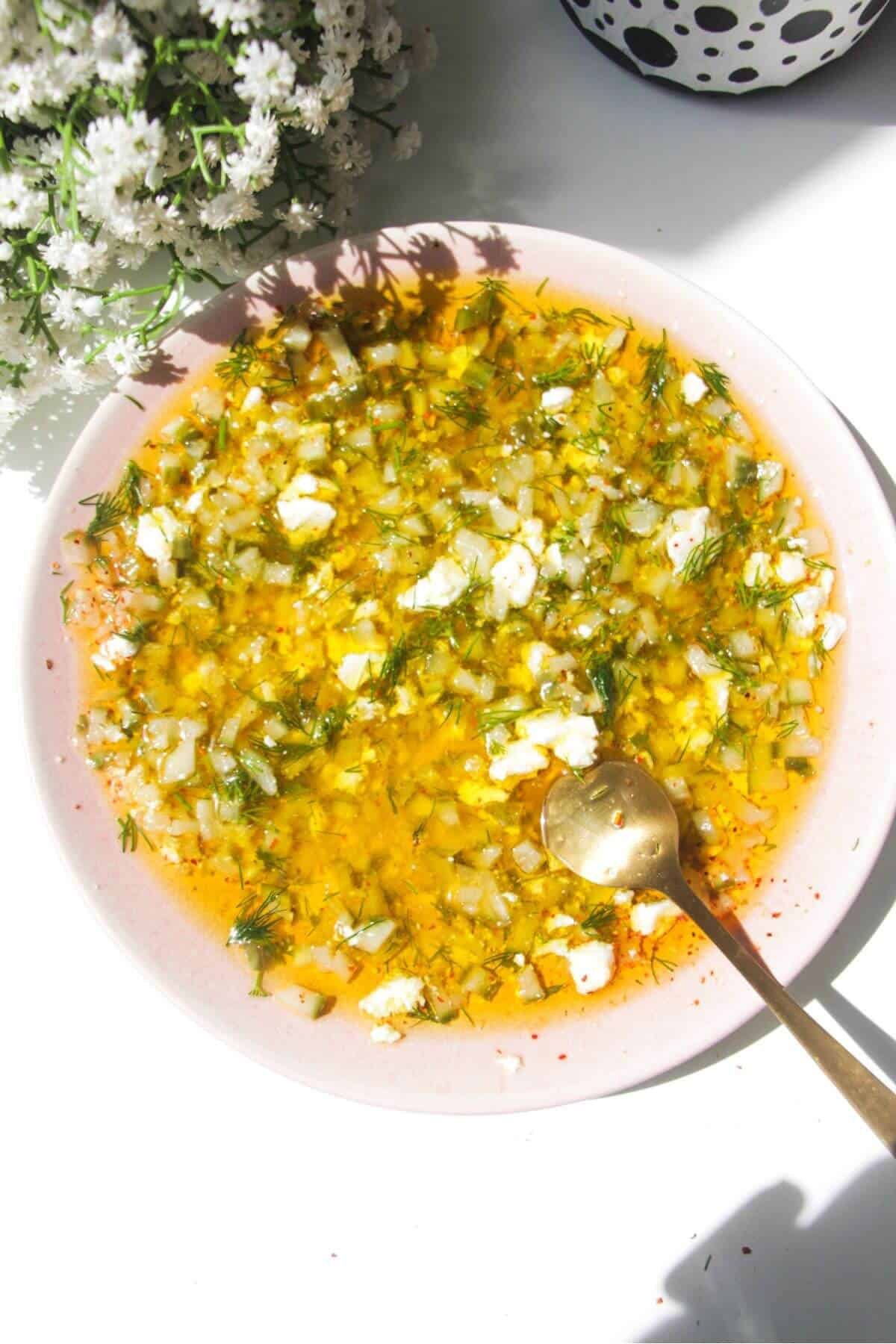 Dill pickle dipping oil mixed in a small pink plate with a gold spoon on the side.
