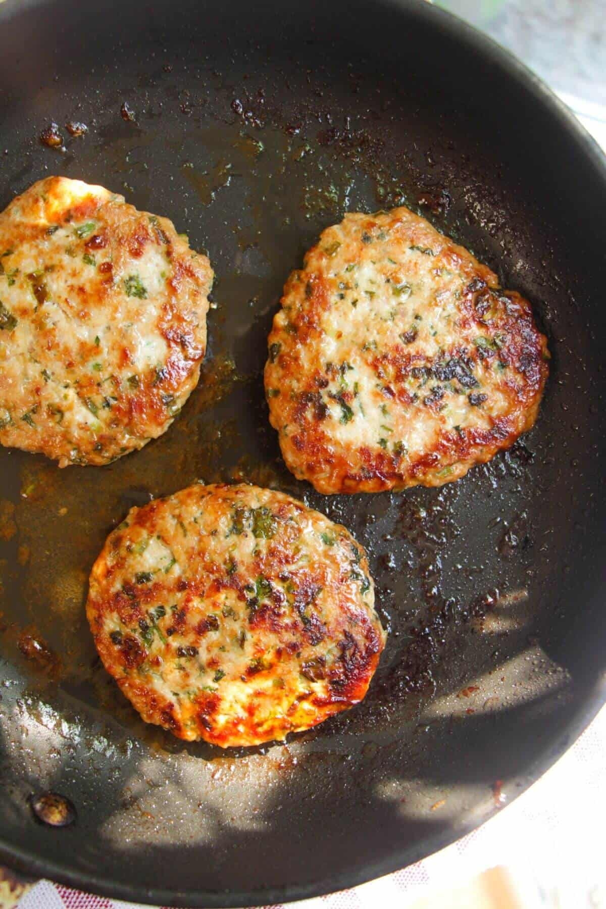 Three dumpling burger patties cooked in a pan.